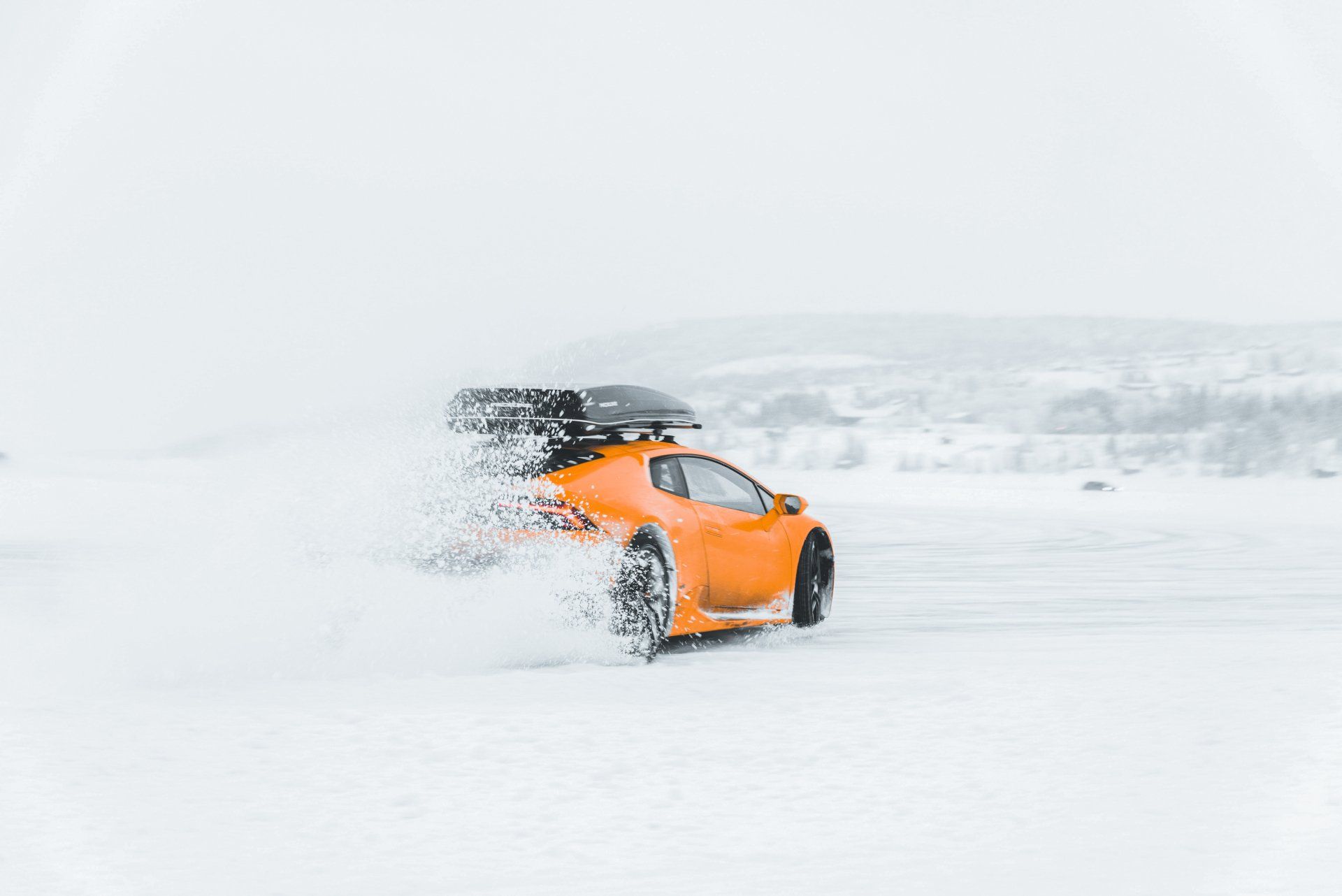 Een oranje lamborghini met een yourroofbox rijdt door de sneeuw.