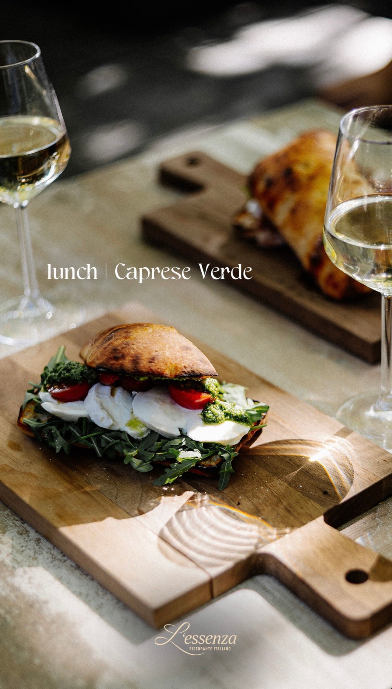 Lunch: Caprese sandwich op een houten plank, met glazen witte wijn.