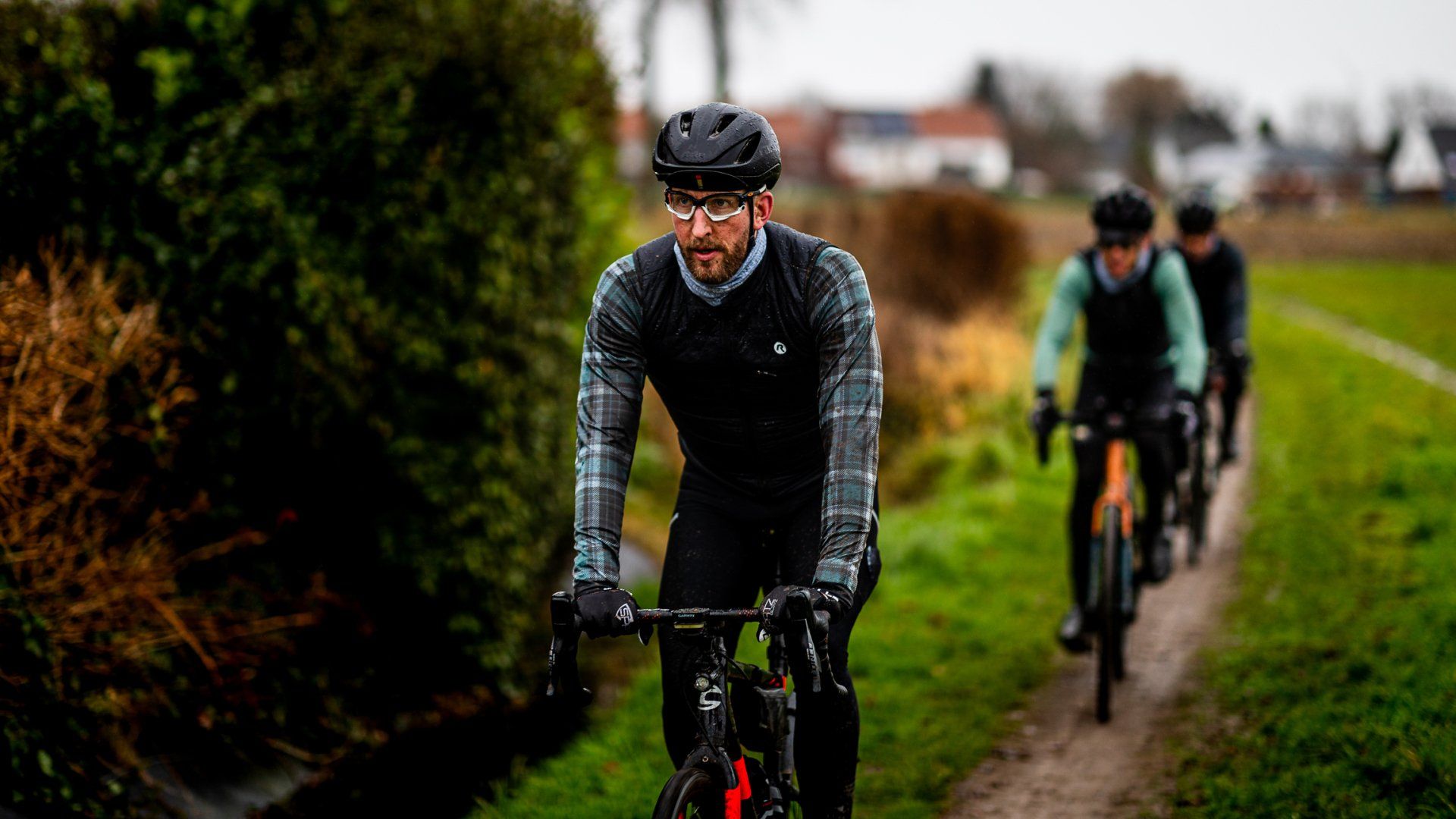 Fietsers rijden op een fietspad, de voorste fietser draagt een shirt met een patroon, groen aan de zijkant, bewolkte dag.