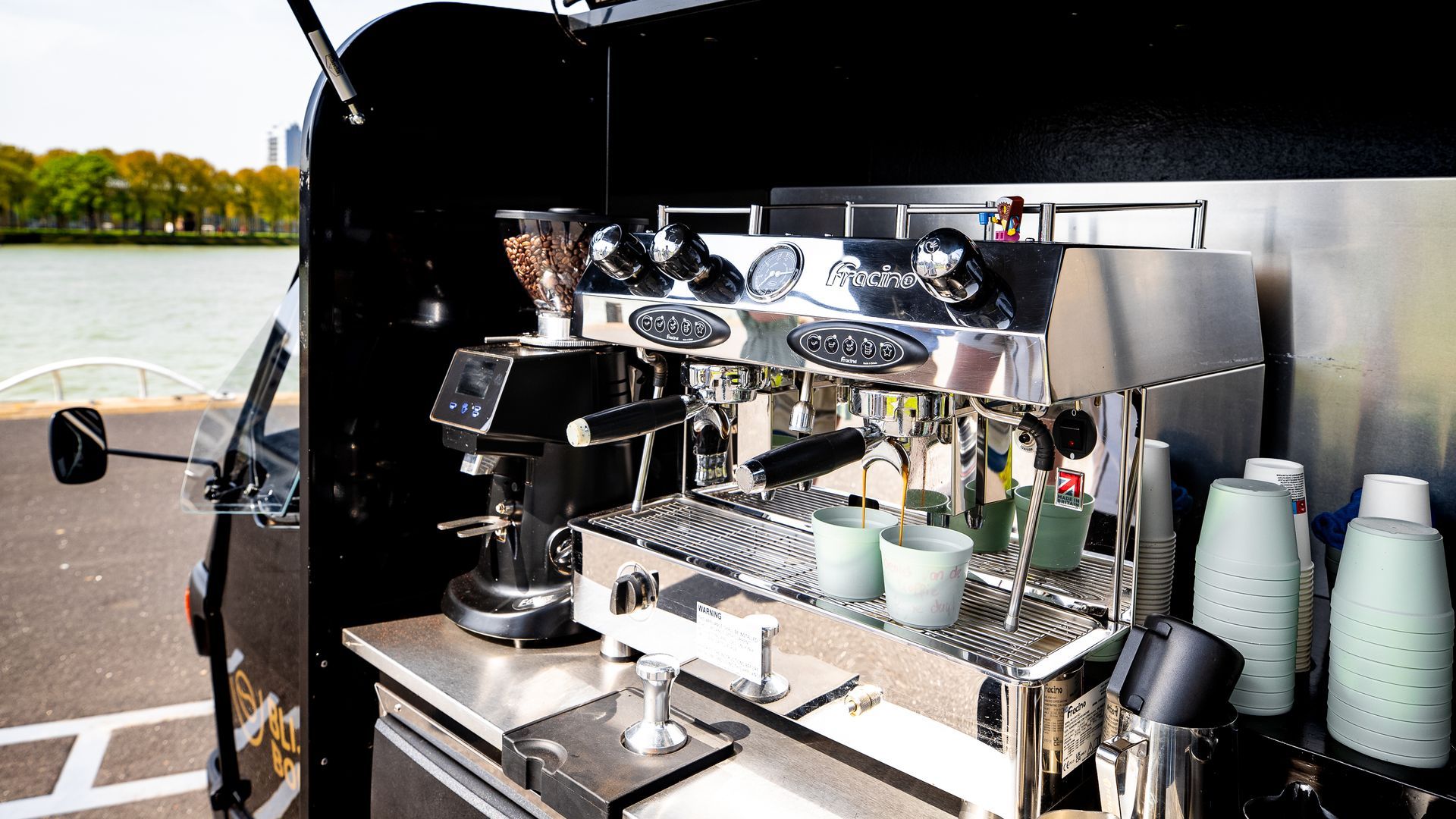 Espressomachine in een zwarte foodtruck, rivier op de achtergrond.