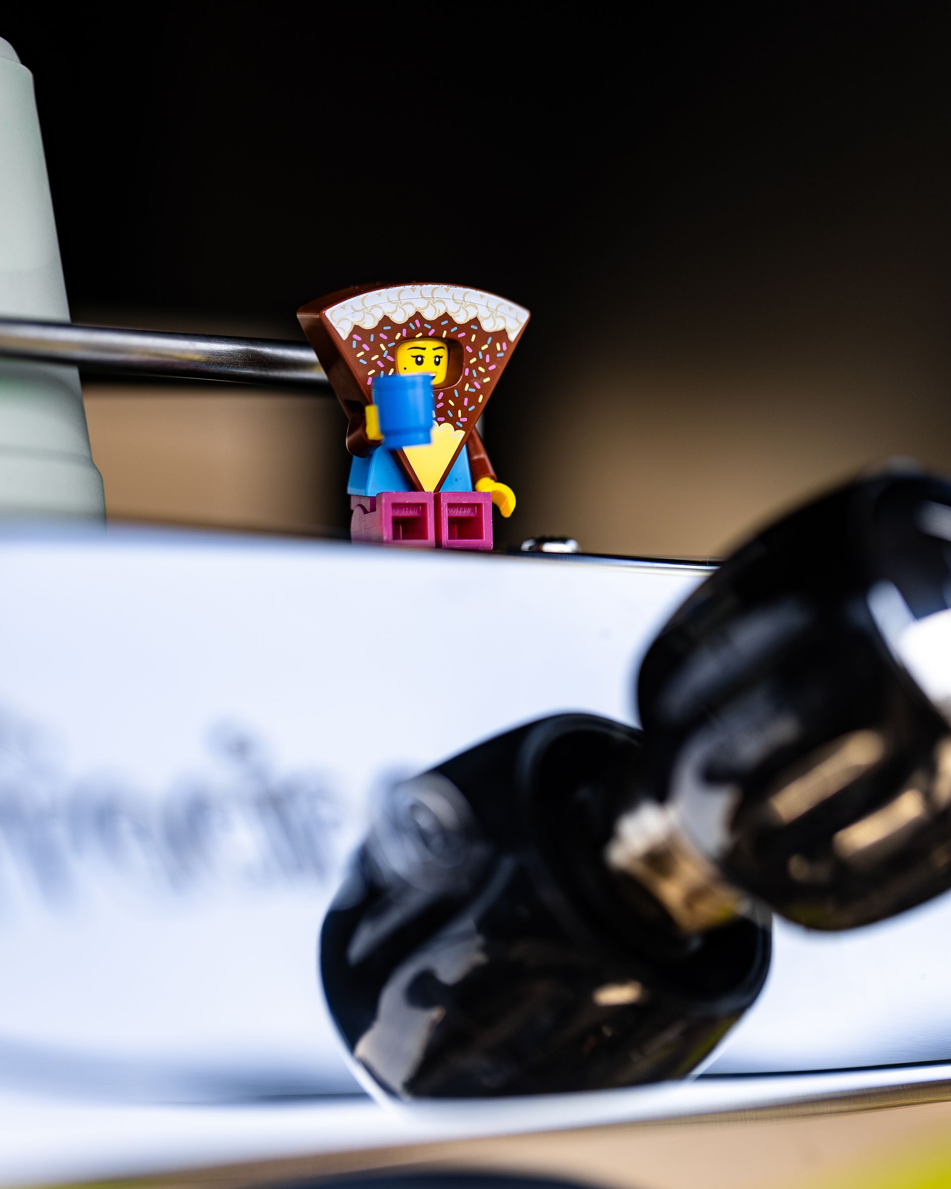 Een Lego-figuurtje zit op een witte ondergrond en leest een blauw boek, met zwarte knoppen op de voorgrond.