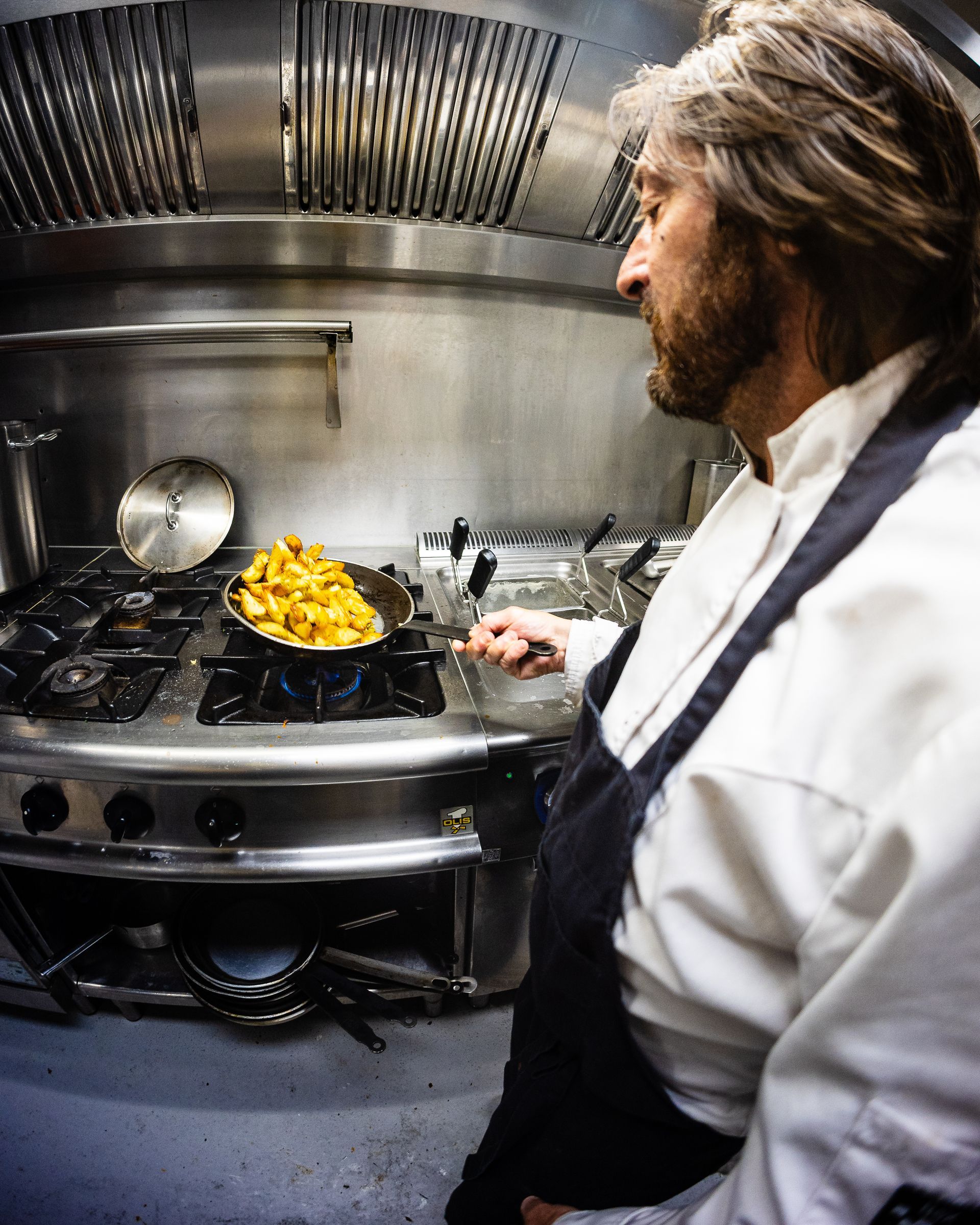 Een chef-kok die kookt in een professionele keuken; eten dat sist in een pan boven een gasbrander.