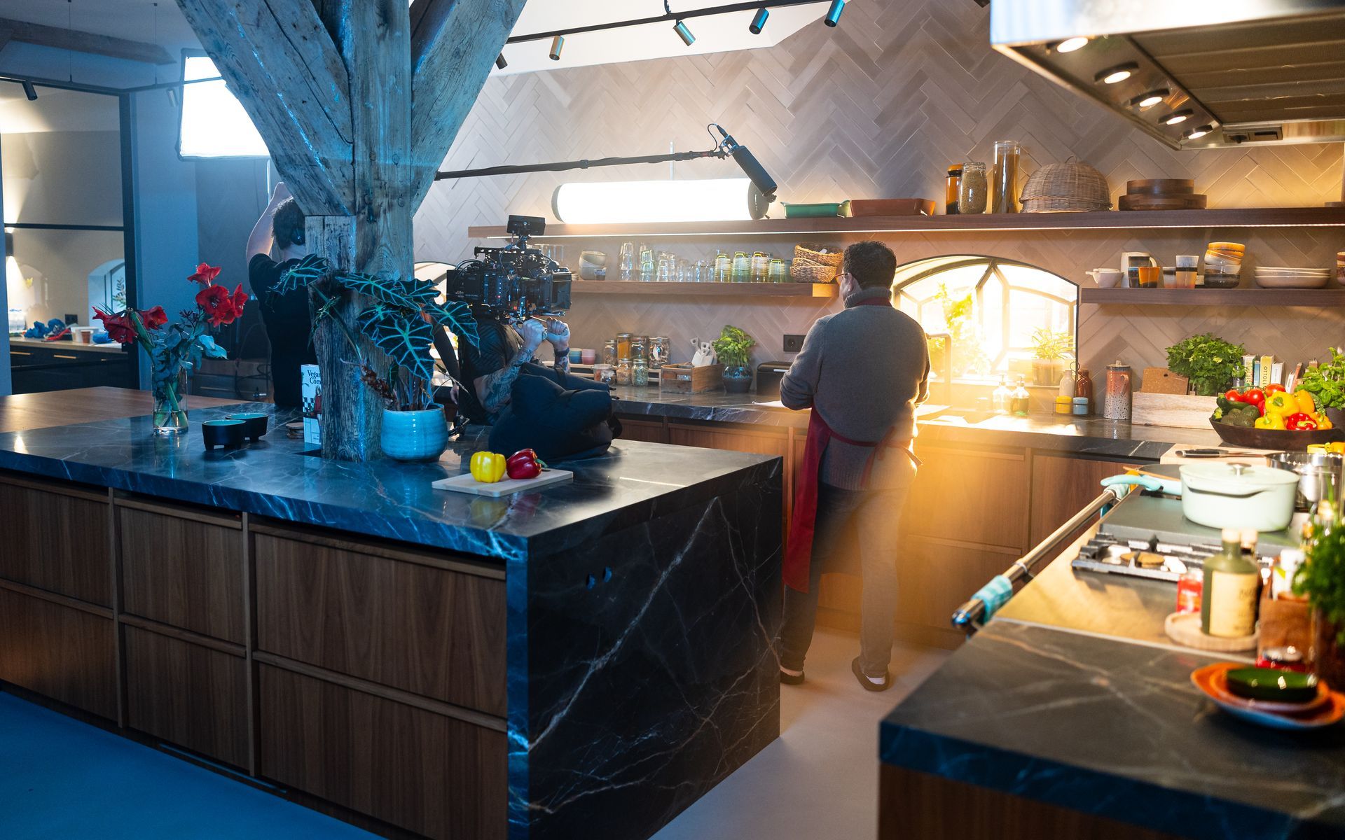 Keuken met chef-kok, marmeren aanrechtbladen, houten kasten en planken vol met etenswaren en apparatuur.