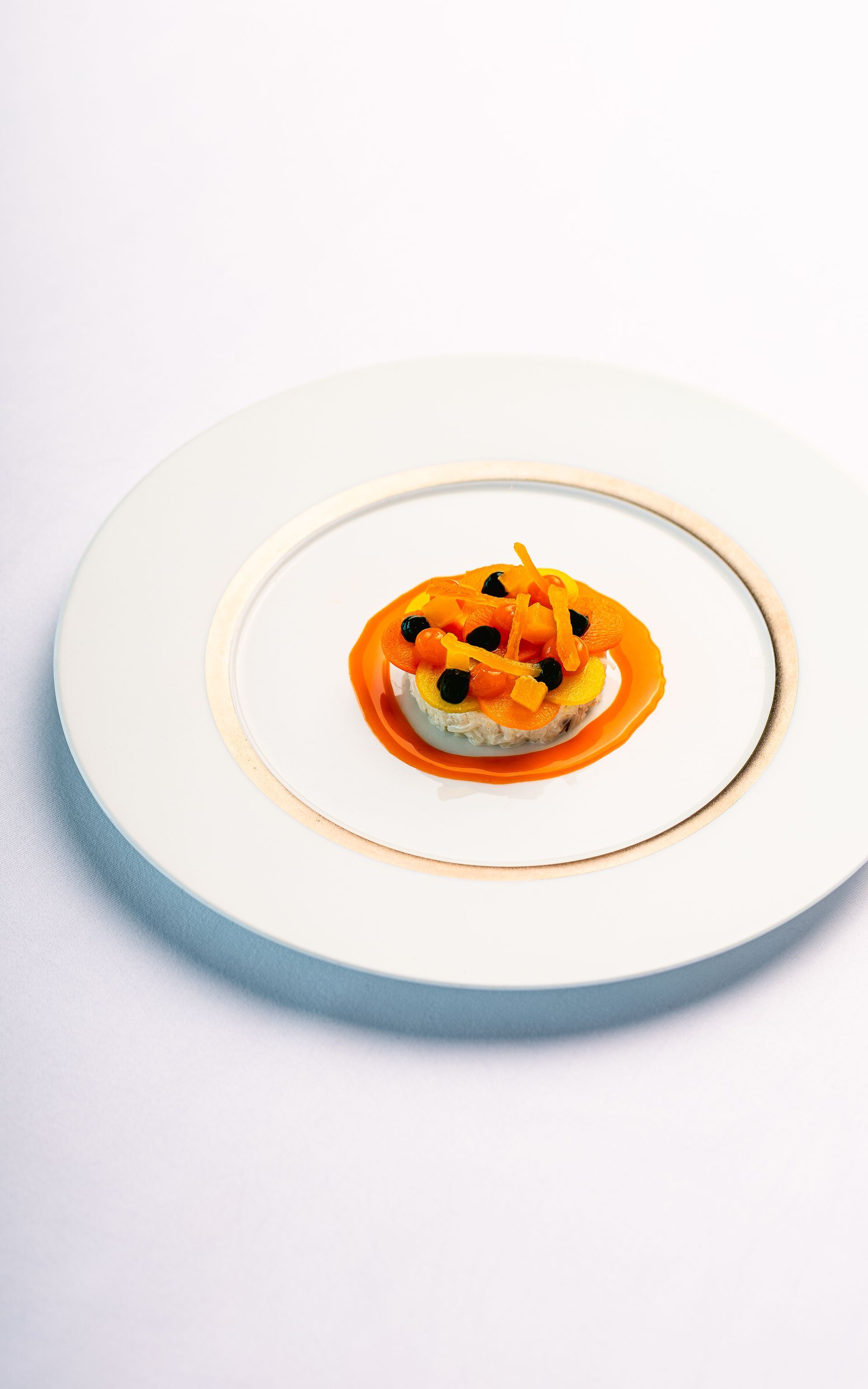 Elegant gerecht op een wit bord: rond, gestapeld voedsel met sinaasappelsaus en topping.