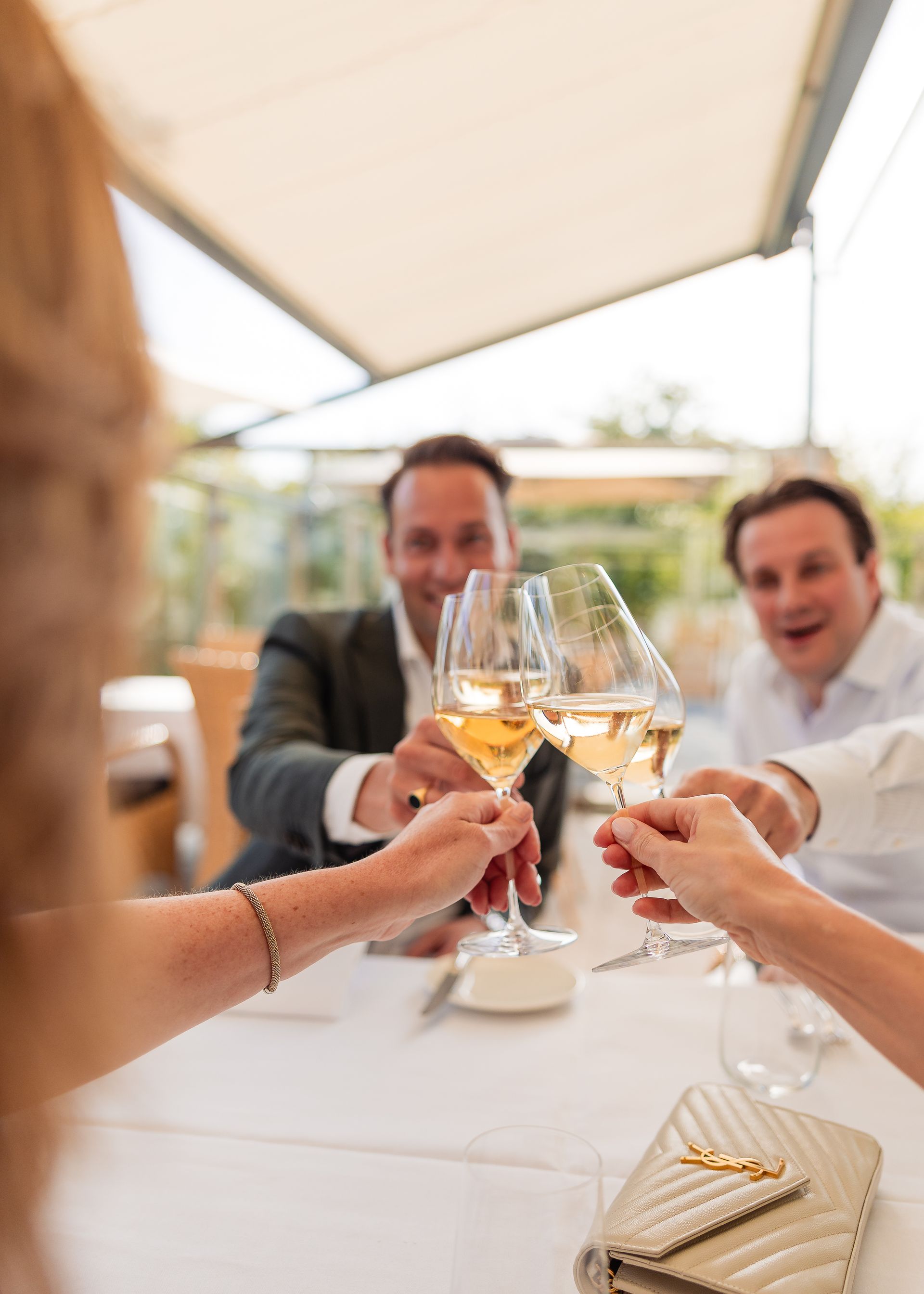 Mensen die met wijnglazen proosten aan een tafeltje op het terras van een restaurant.