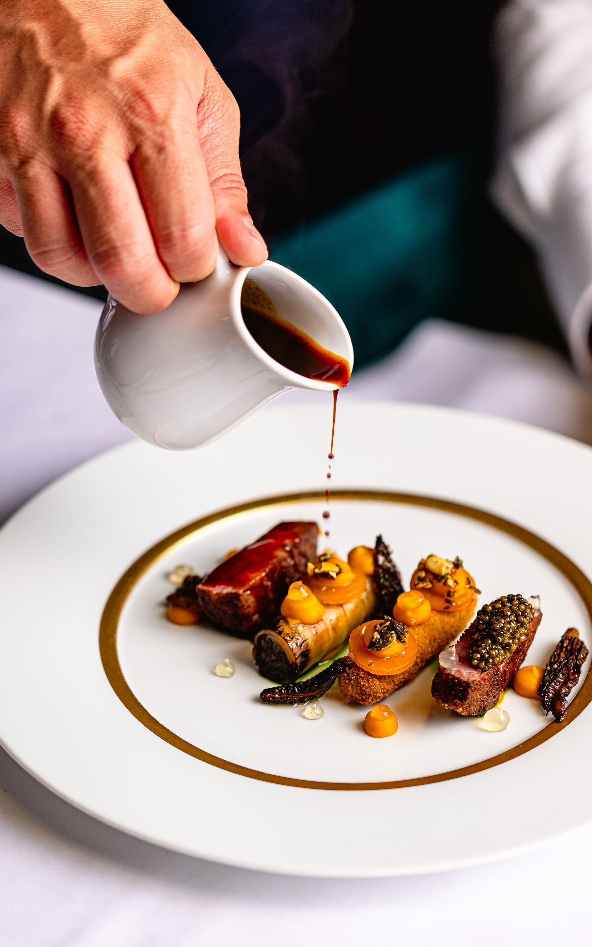 De chef-kok giet saus over een op een bord geserveerd gerecht met geroosterde groenten en vlees.