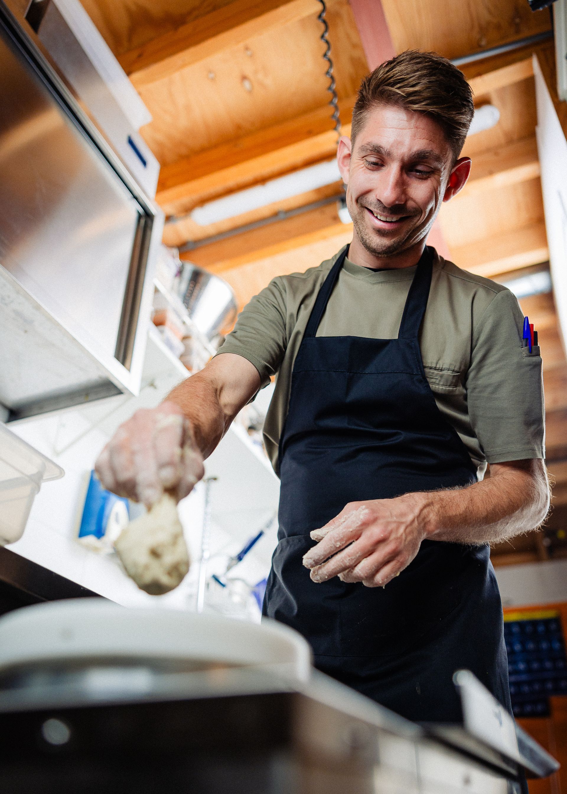 Een chef-kok met een schort om staat te lachen terwijl hij met deeg bezig is.