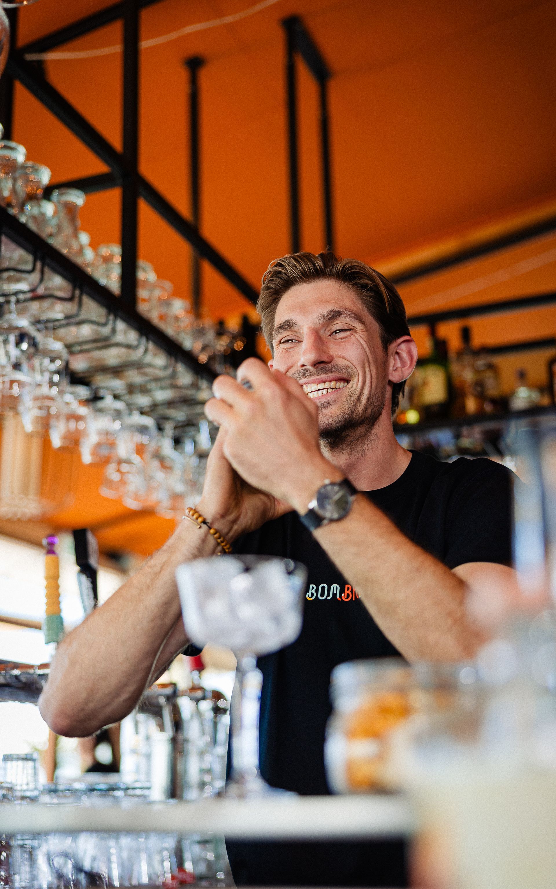 Een glimlachende barman schudt met een cocktailshaker. Drankjes, glazen en de bar zelf.