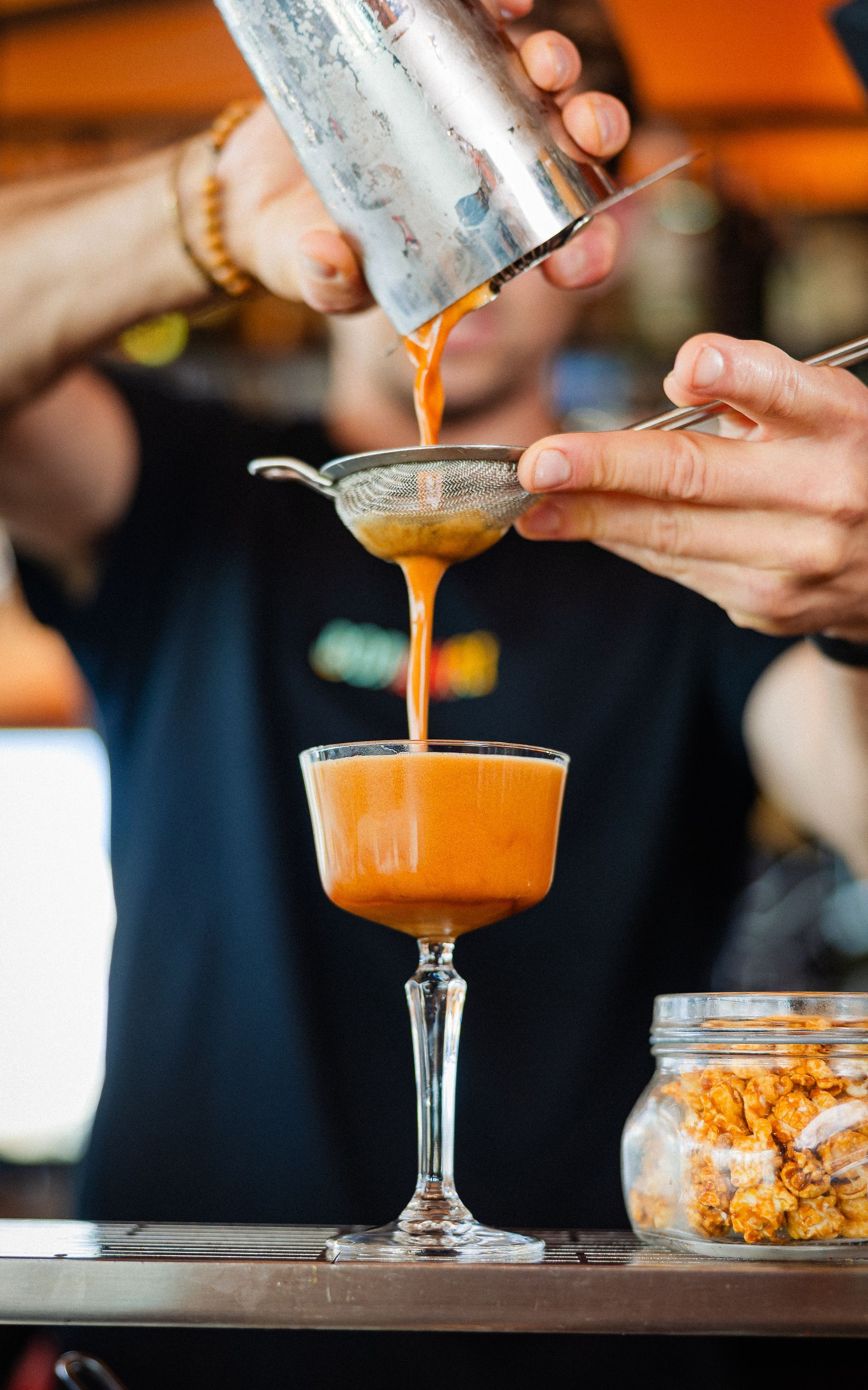 De barman schenkt een sinaasappelcocktail in een glas op voet, in een barsetting.