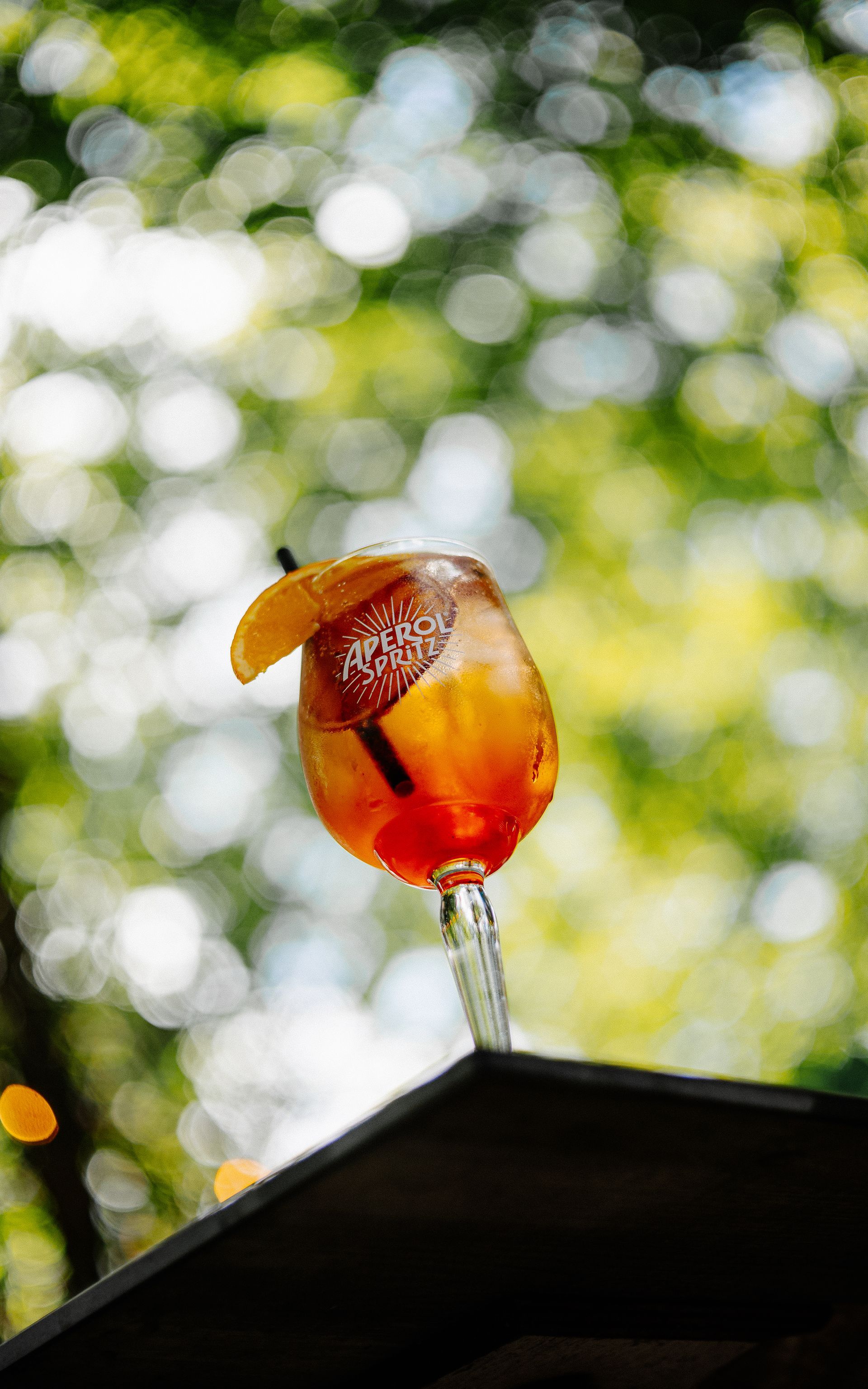 Cocktail in een glas op voet met een schijfje sinaasappel als garnering, wazige groene achtergrond.