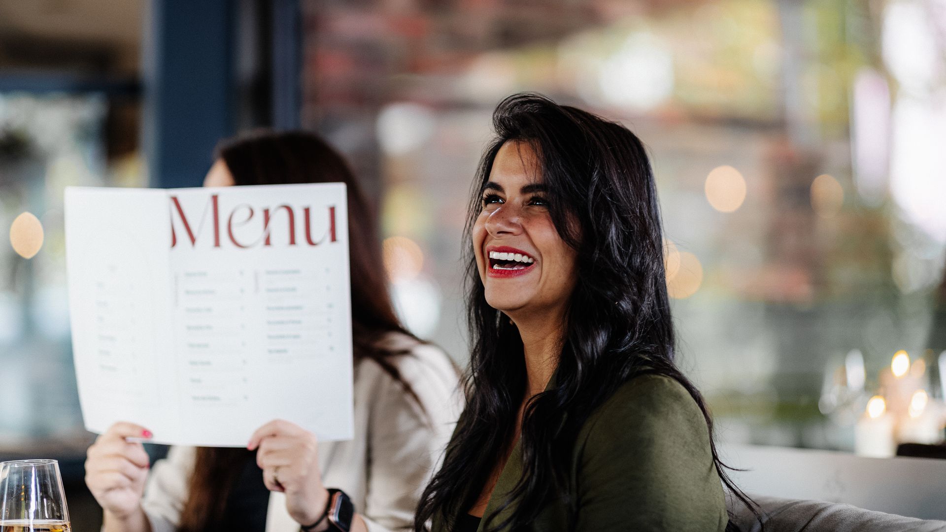 Een vrouw lacht terwijl ze een menukaart in een restaurant vasthoudt.