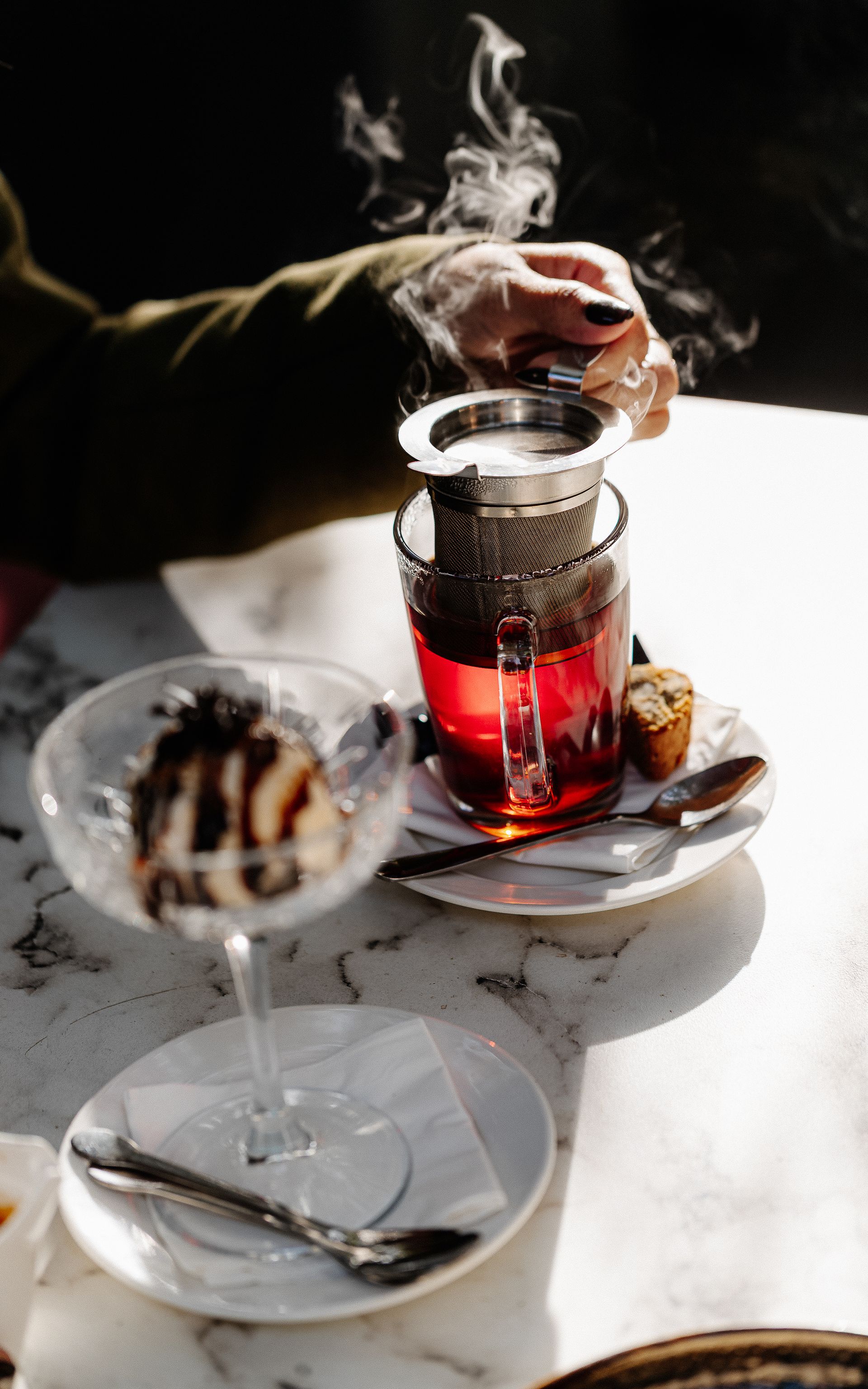 Stoomende rode thee met theefilter, een klein dessert en ijs in een glas op een marmeren tafel.