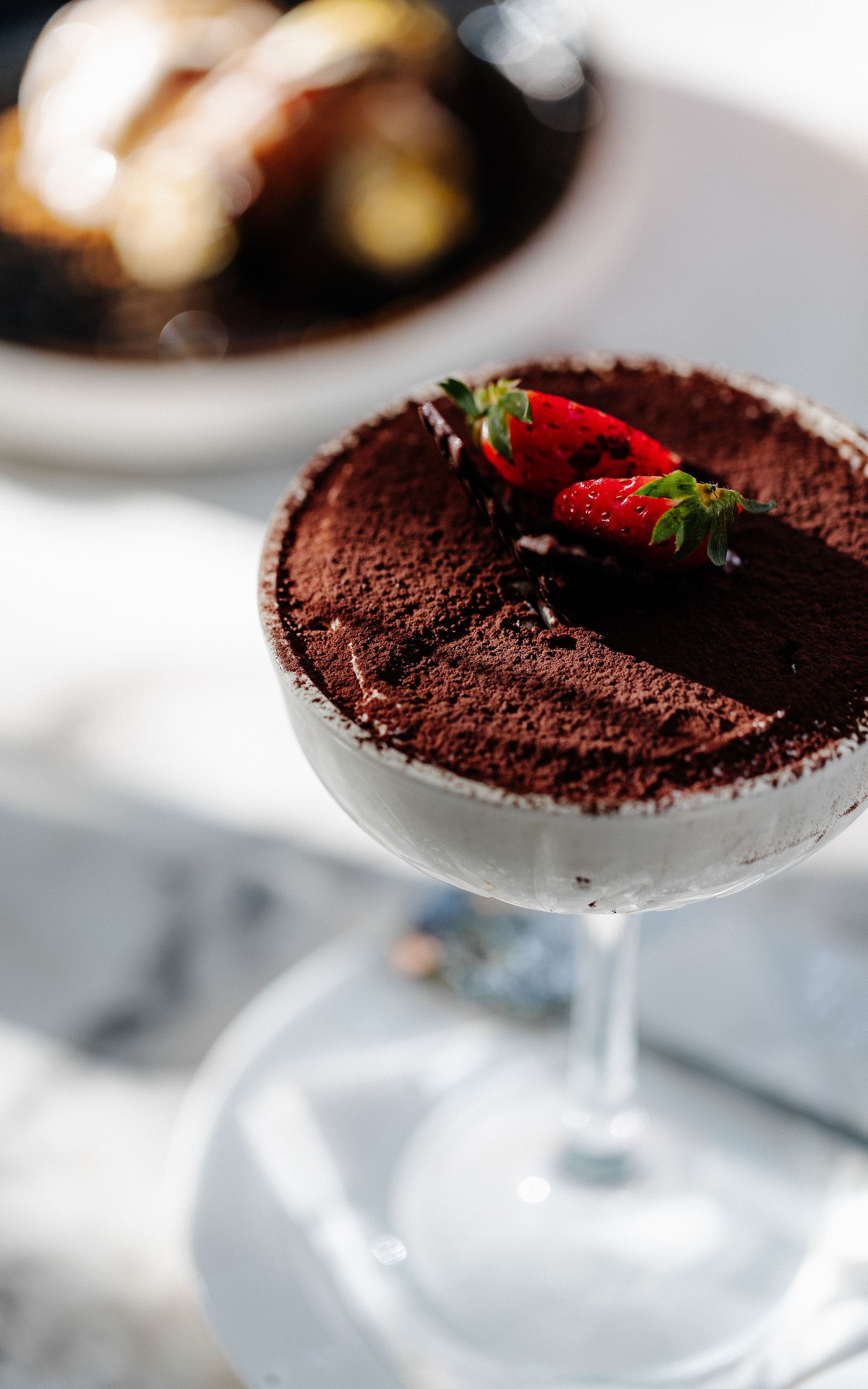 Tiramisu in een glas, bestrooid met cacaopoeder en gegarneerd met twee aardbeien op een witte ondergrond.