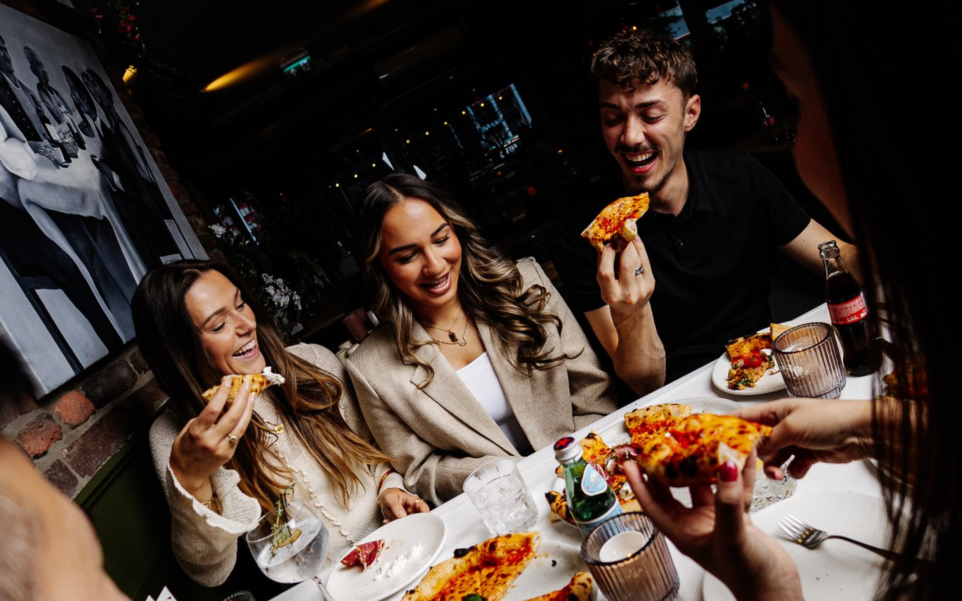 Mensen eten pizza aan een tafel in een restaurant. Ze lachen en hebben contact. Bij L'Essenza Rotterdam.