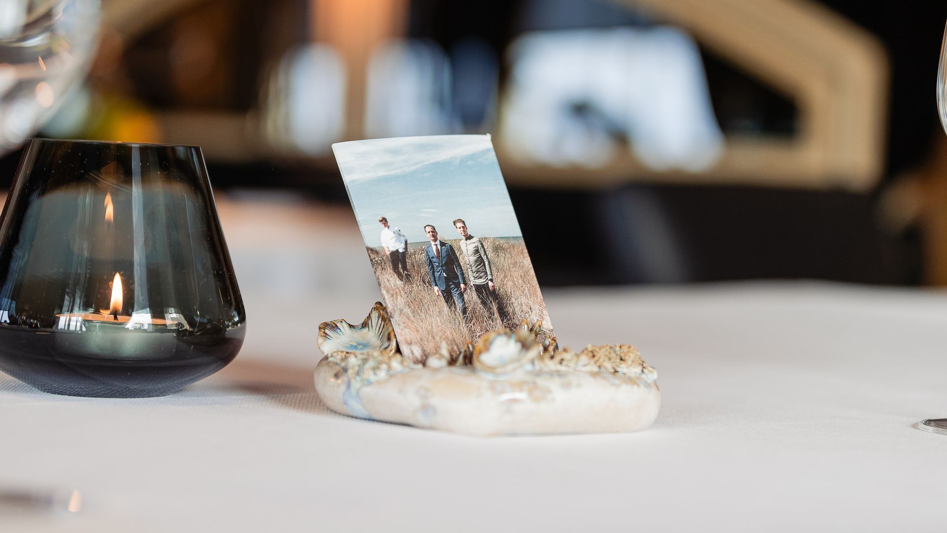 Een fotopresentatie op een tafel, een strandscène in een stenen houder met een kaars in een glazen houder.