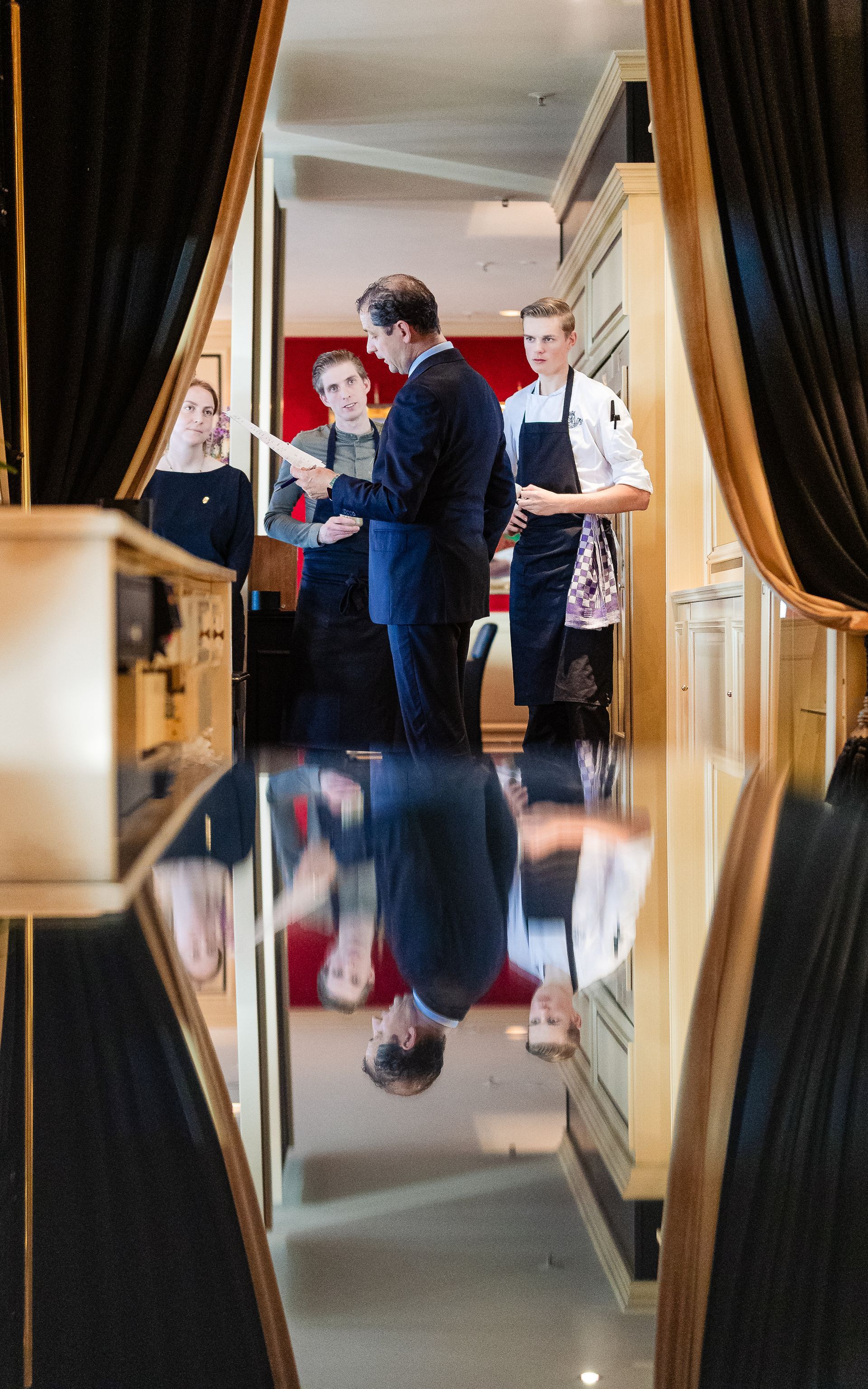 Een man in pak bekijkt documenten met personeel in een restaurantgang met een spiegelende vloer.