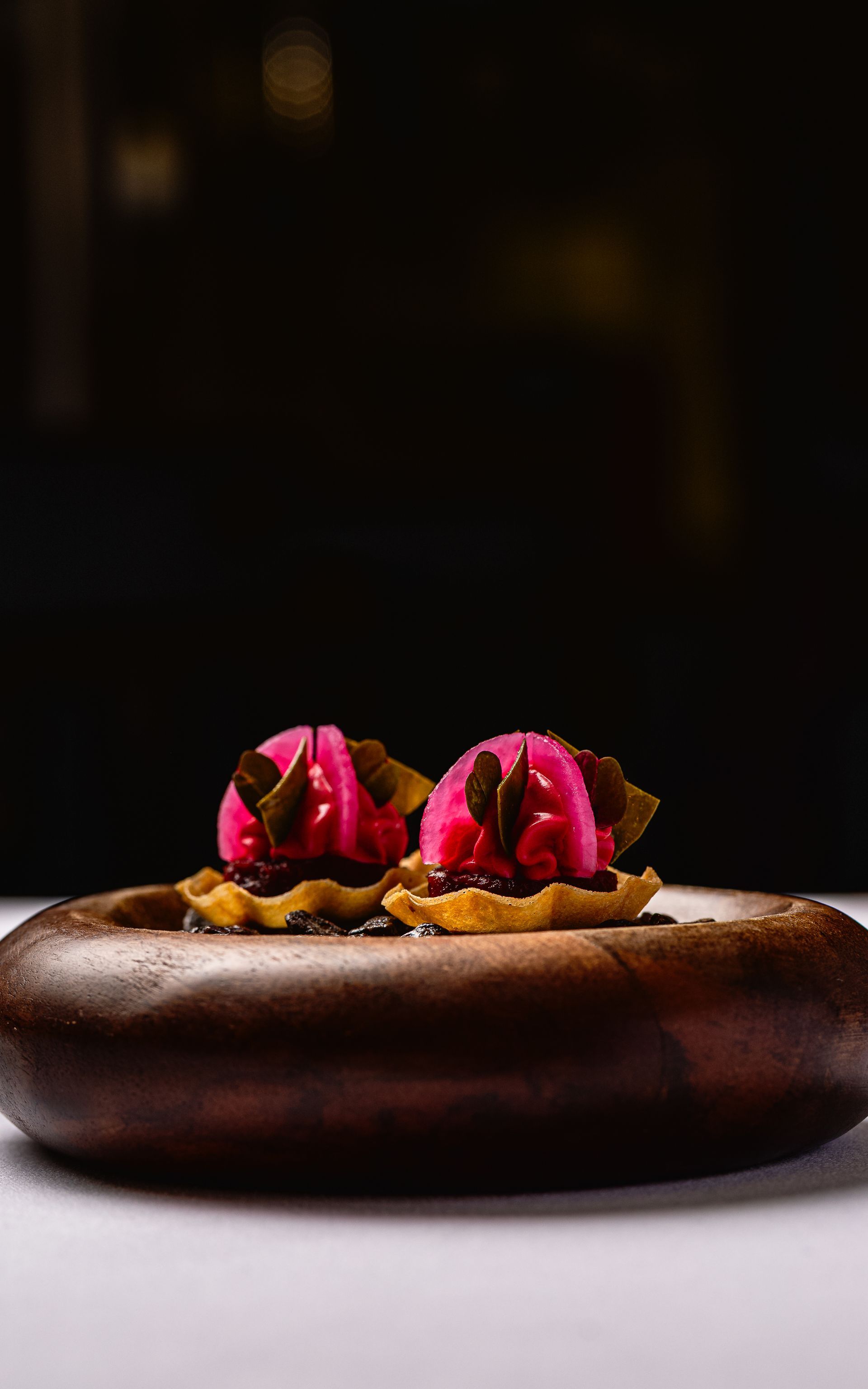 Twee roze chocoladetaartjes op een houten bord, tegen een donkere achtergrond.