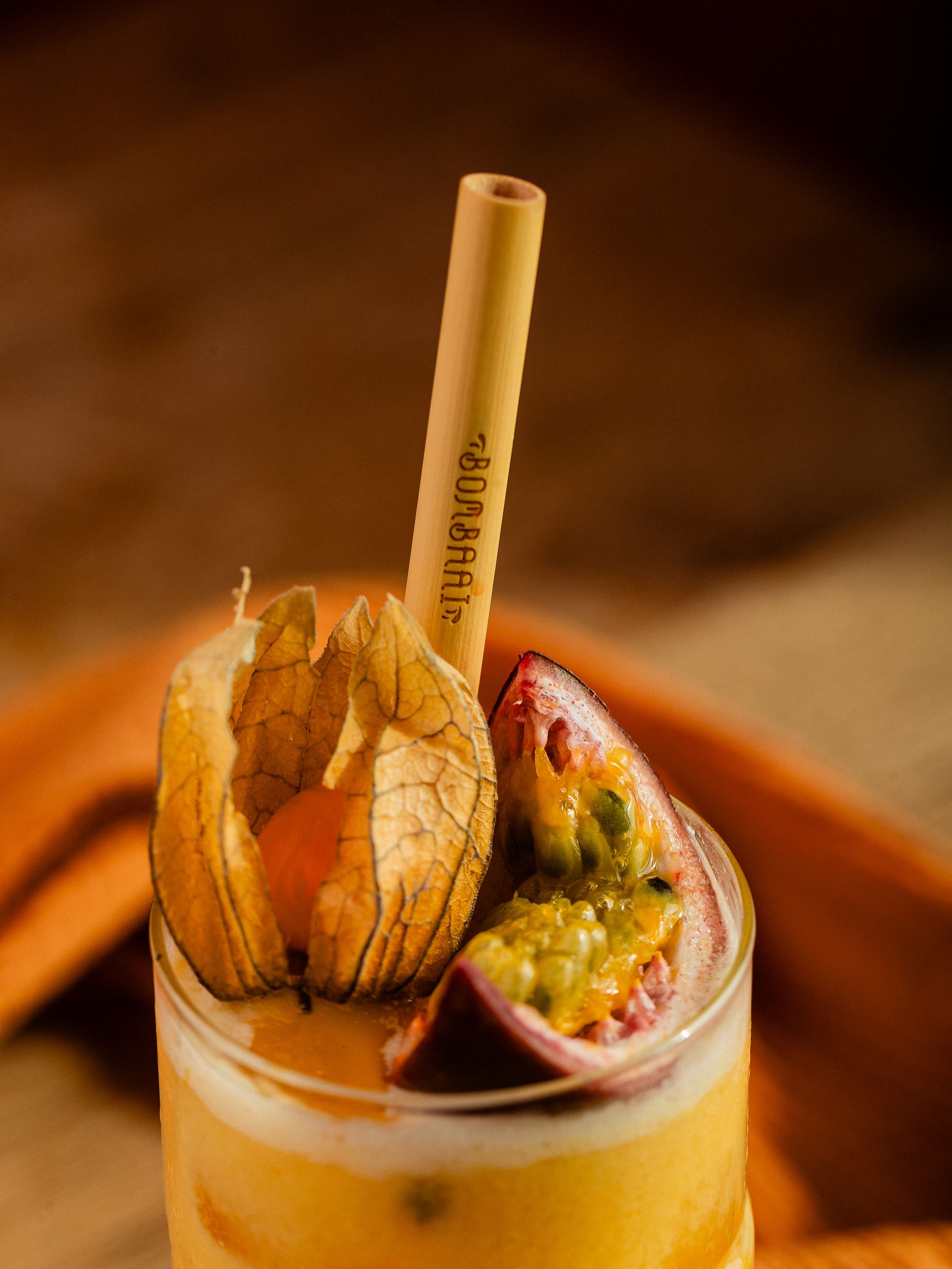 Cocktail met een schijfje passievrucht, kruisbes en bamboerietje. Oranje en gele tinten.