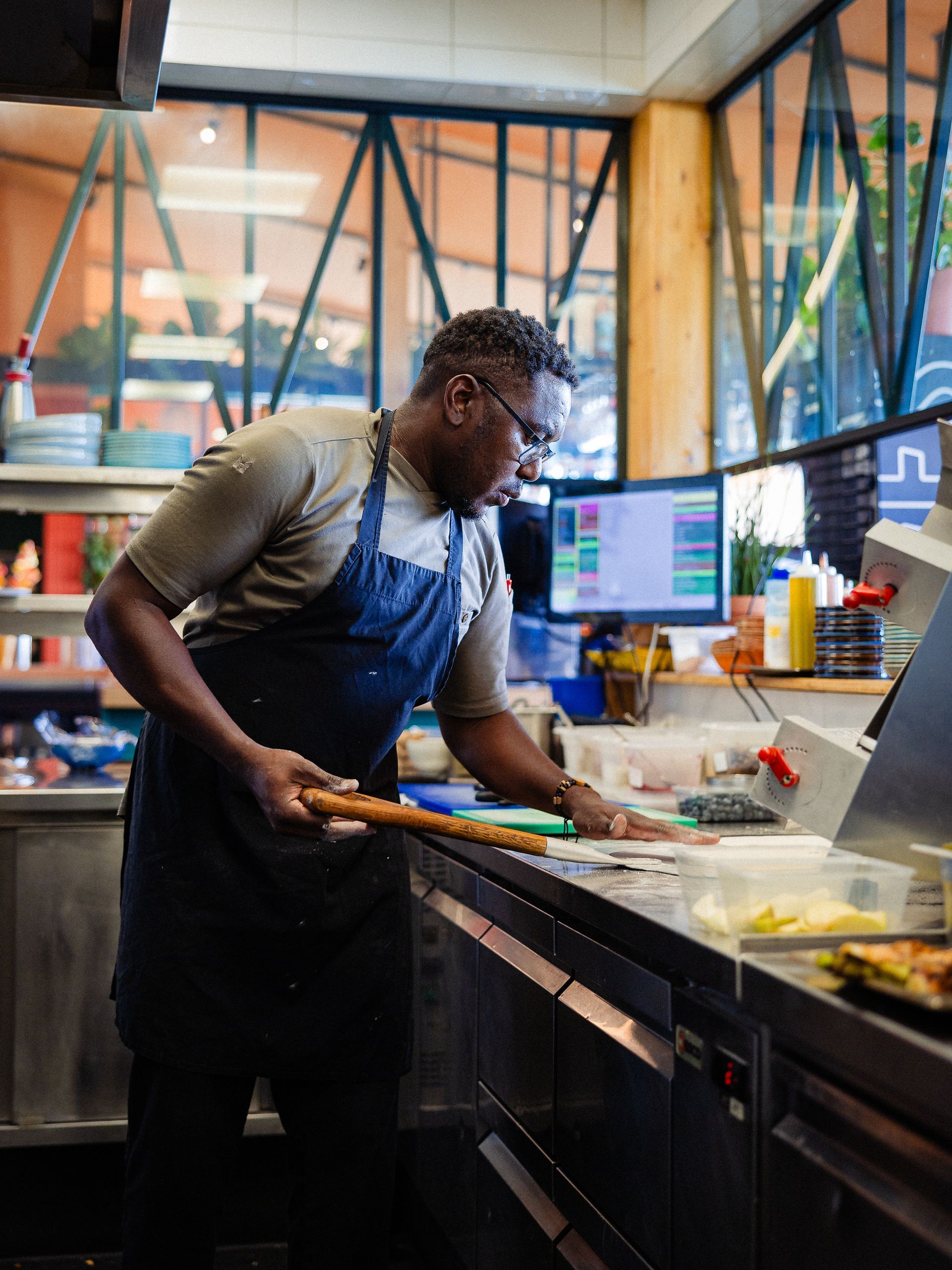 Een chef-kok met een blauw schort inspecteert het eten op een aanrecht in een lichte keuken.