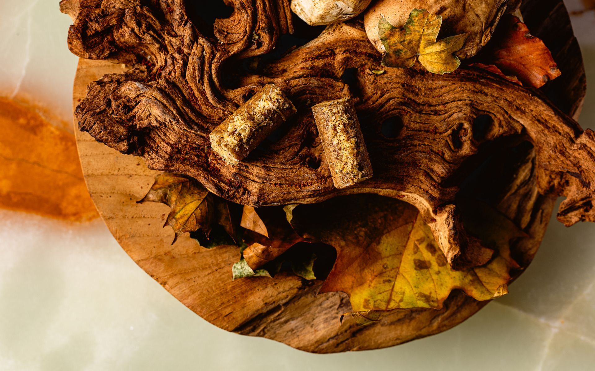 Houten plank met kurken, herfstbladeren en mogelijk paddenstoelen, op een lichtgekleurde ondergrond.