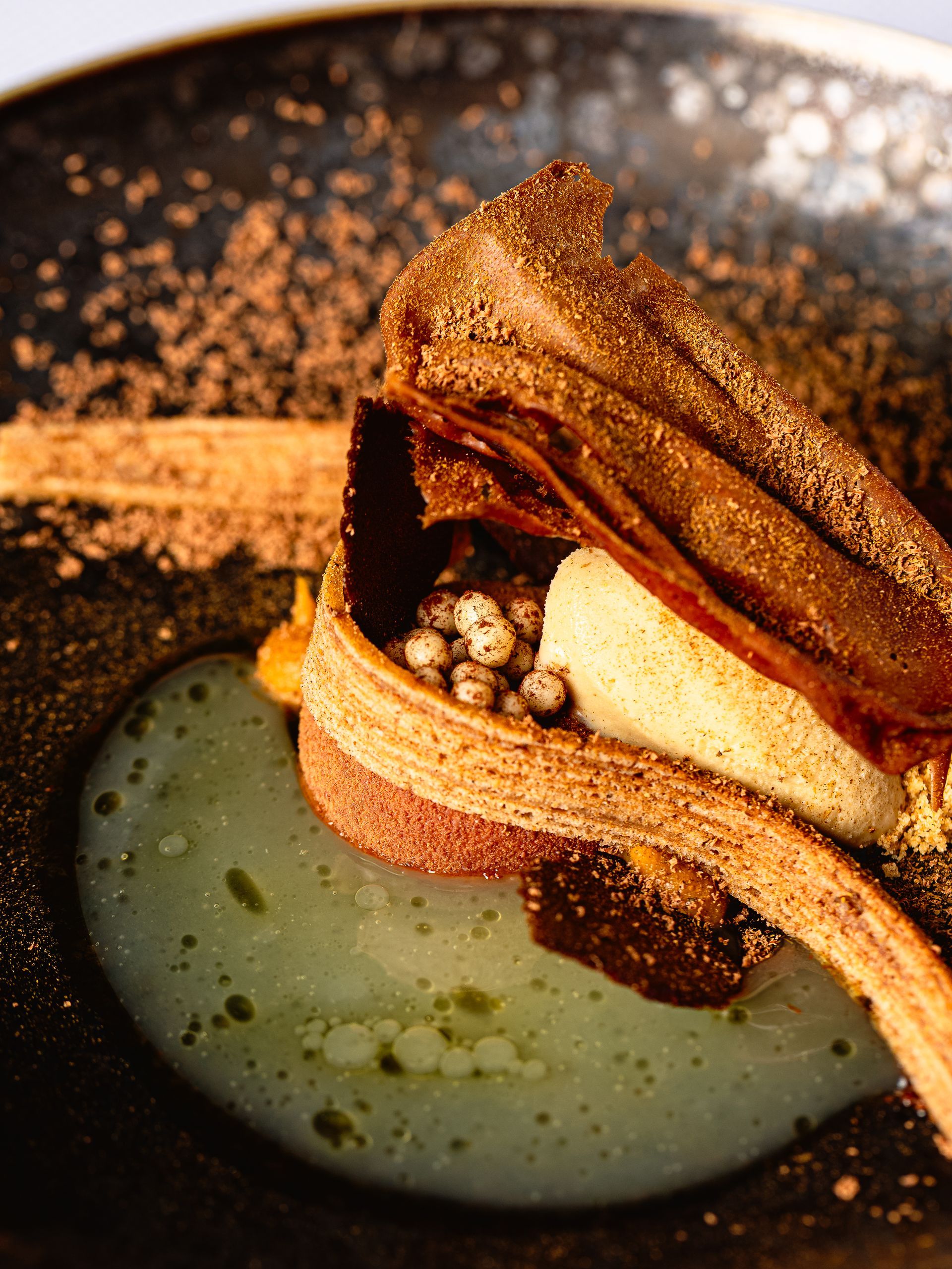 Een gastronomisch dessert in een donkere kom: laagjes bladerdeeg, schuim en chocoladepoeder.