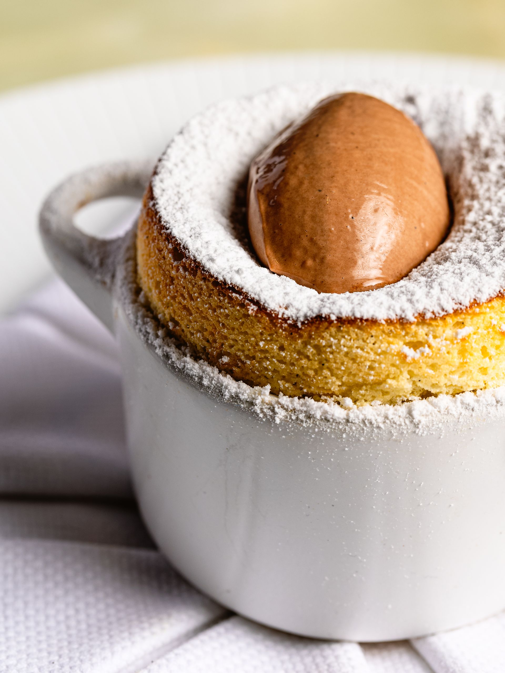 Soufflé met chocolade-ijs in een witte keramische schaal, bestrooid met poedersuiker.
