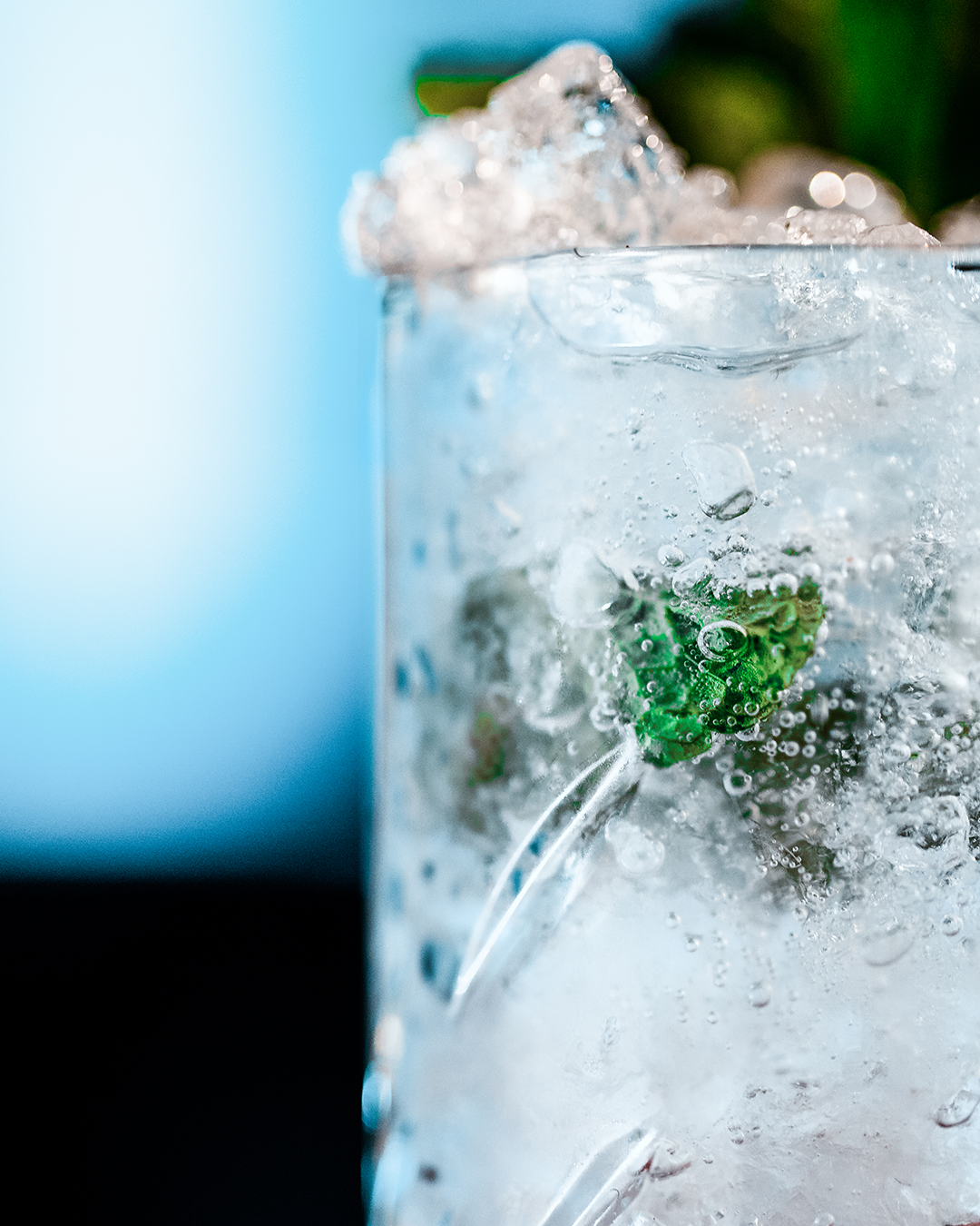 Close-up van een heldere cocktail in een glas, met muntblaadjes, ijs en bubbels.