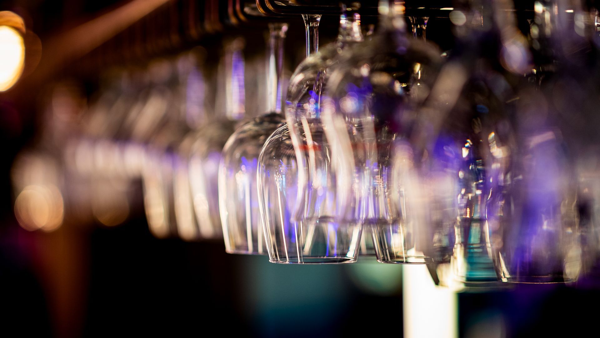 Wijnglazen hangen ondersteboven in een bar. Zachte verlichting met een wazige achtergrond.