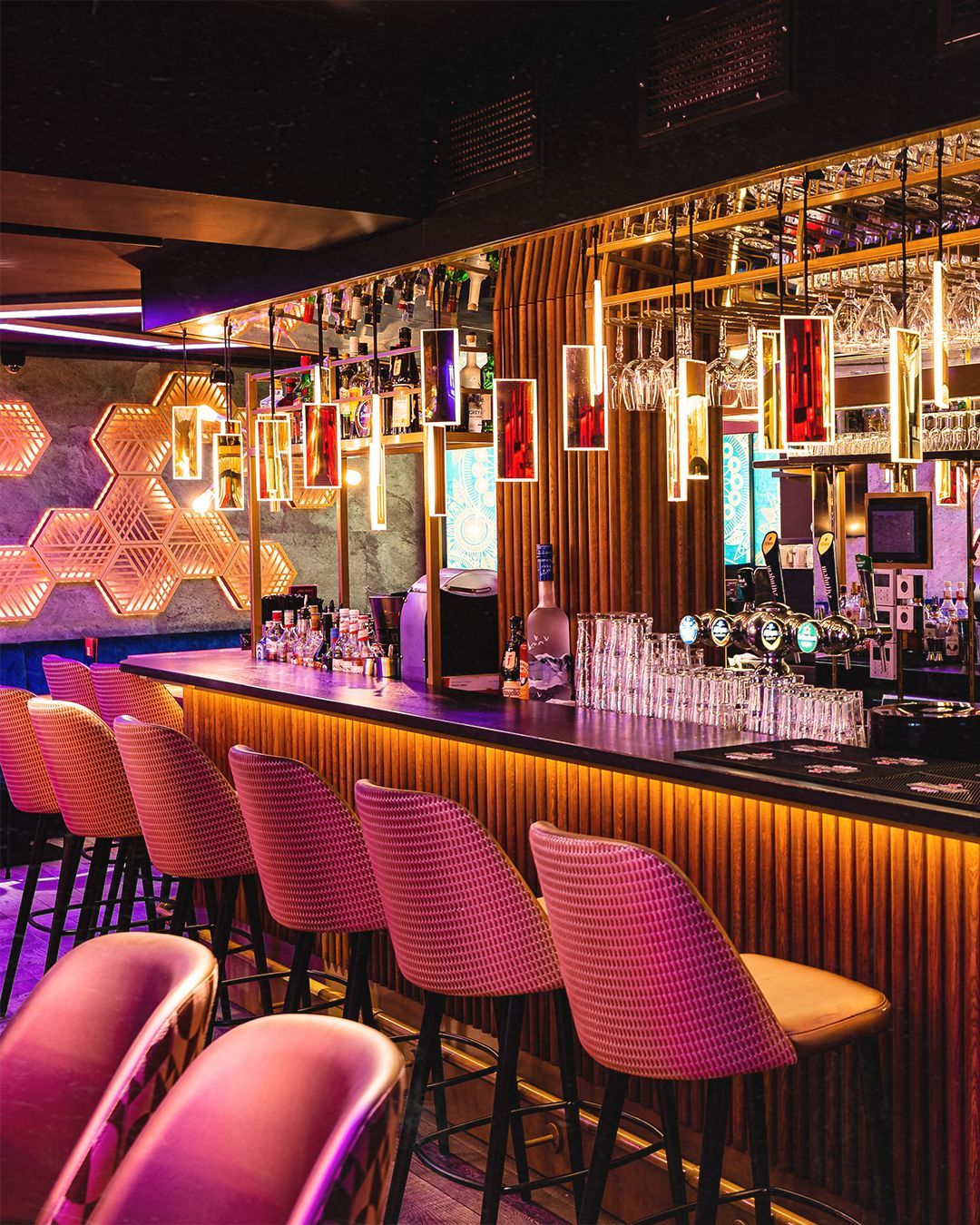 Bar met roze zitjes, gouden accenten en flessen achter de toonbank.