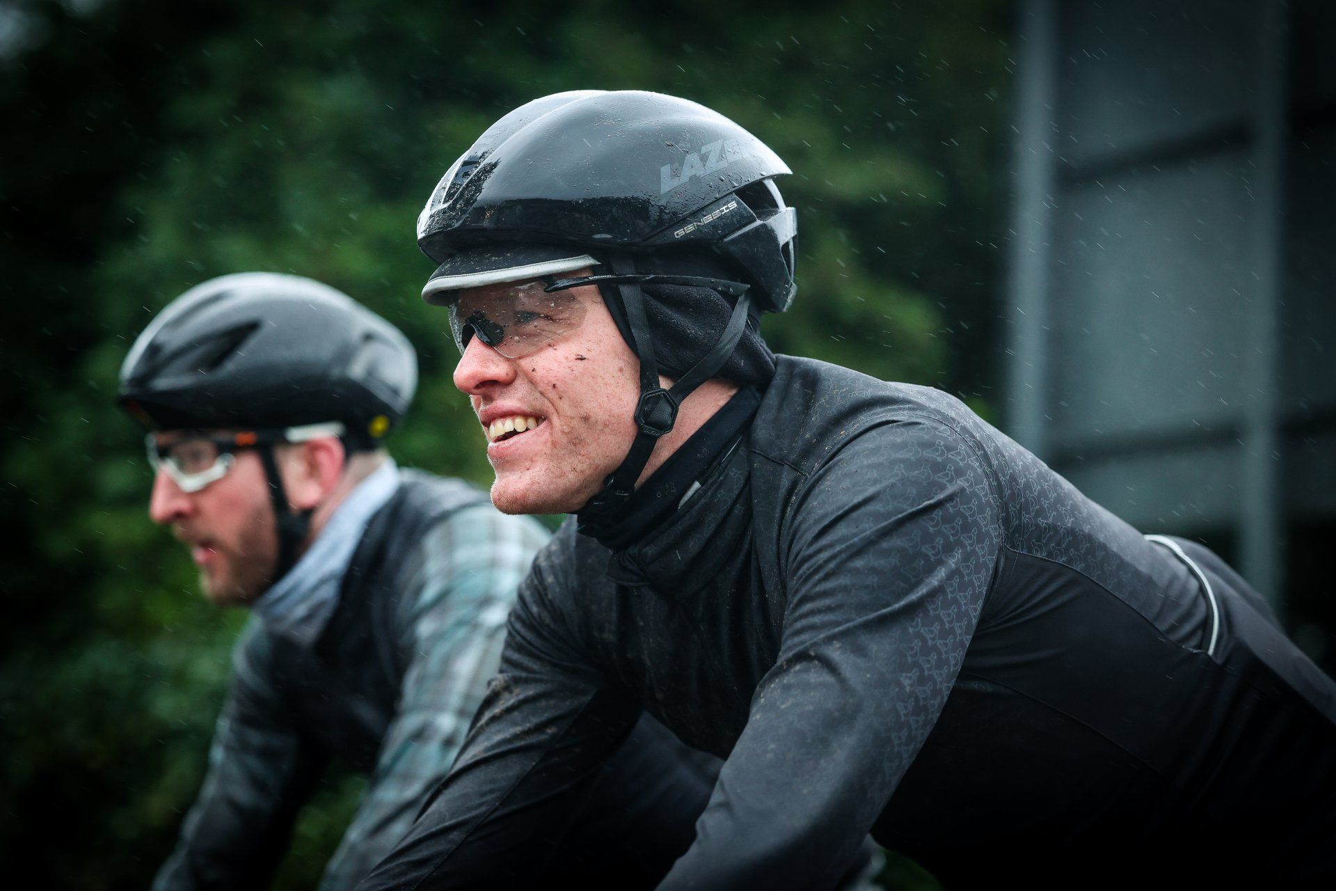 Twee fietsers in zwarte regenkleding en helmen rijden in de regen.