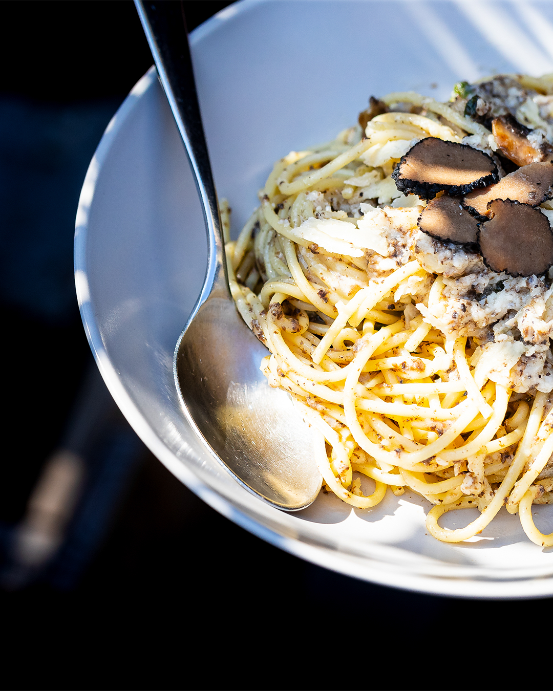 Spaghetti met truffelschijfjes in een witte kom, geserveerd met een zilveren lepel.