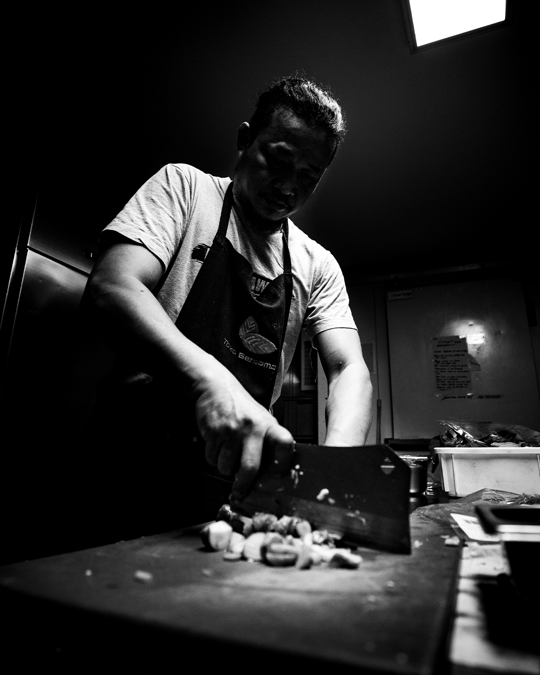 Een chef-kok snijdt ingrediënten op een snijplank in een schemerig verlichte keuken.