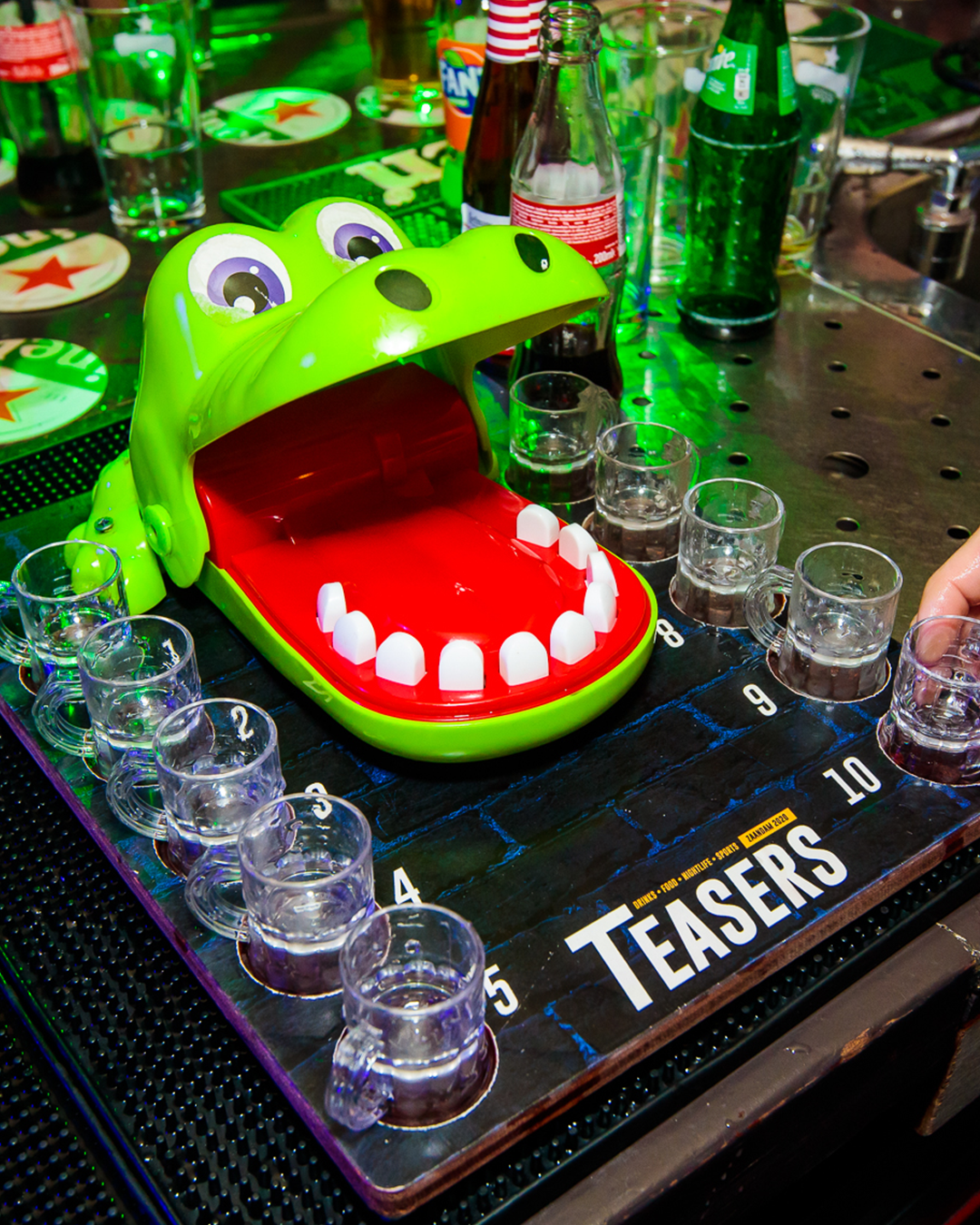 Groen, krokodilvormig drankspel met shotglaasjes op een bar.
