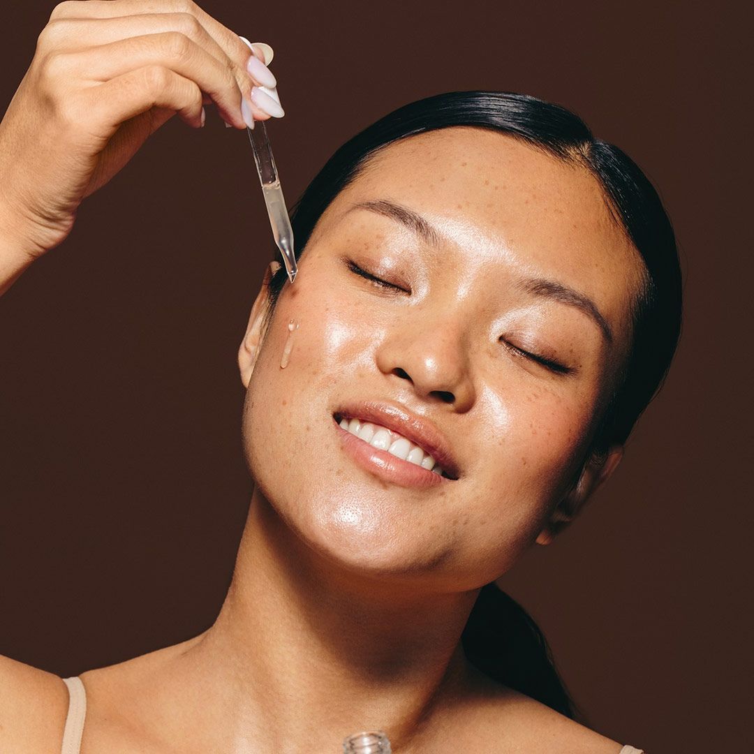 A Woman Is Applying A Serum To Her Face With A Pipette — Chez Belle Skin Care & Beauty Centre in Pimlico, QLD