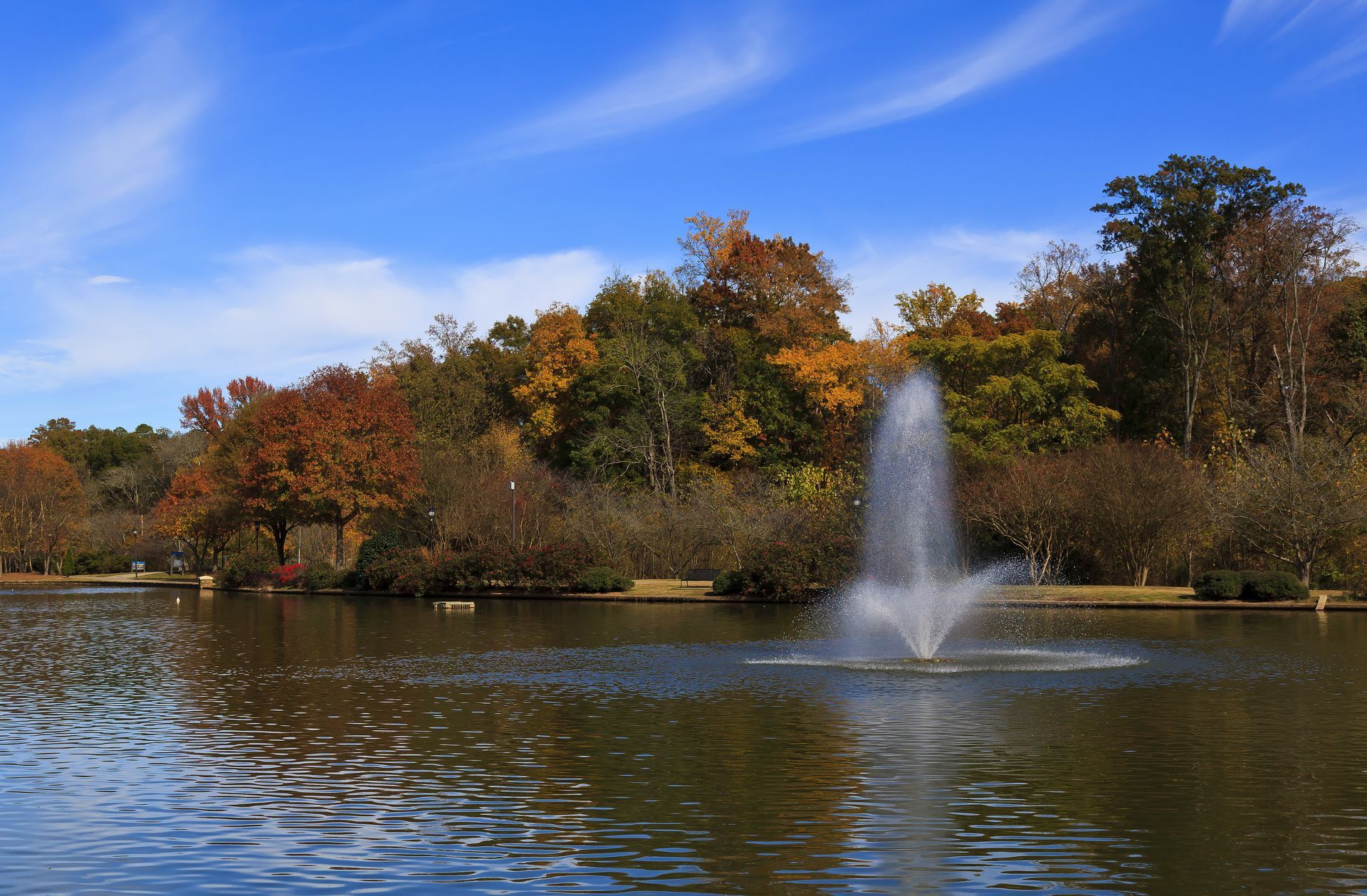 Fountain in a lake with autumn trees under a blue sky at Freedom Park in Dilworth, Charlotte