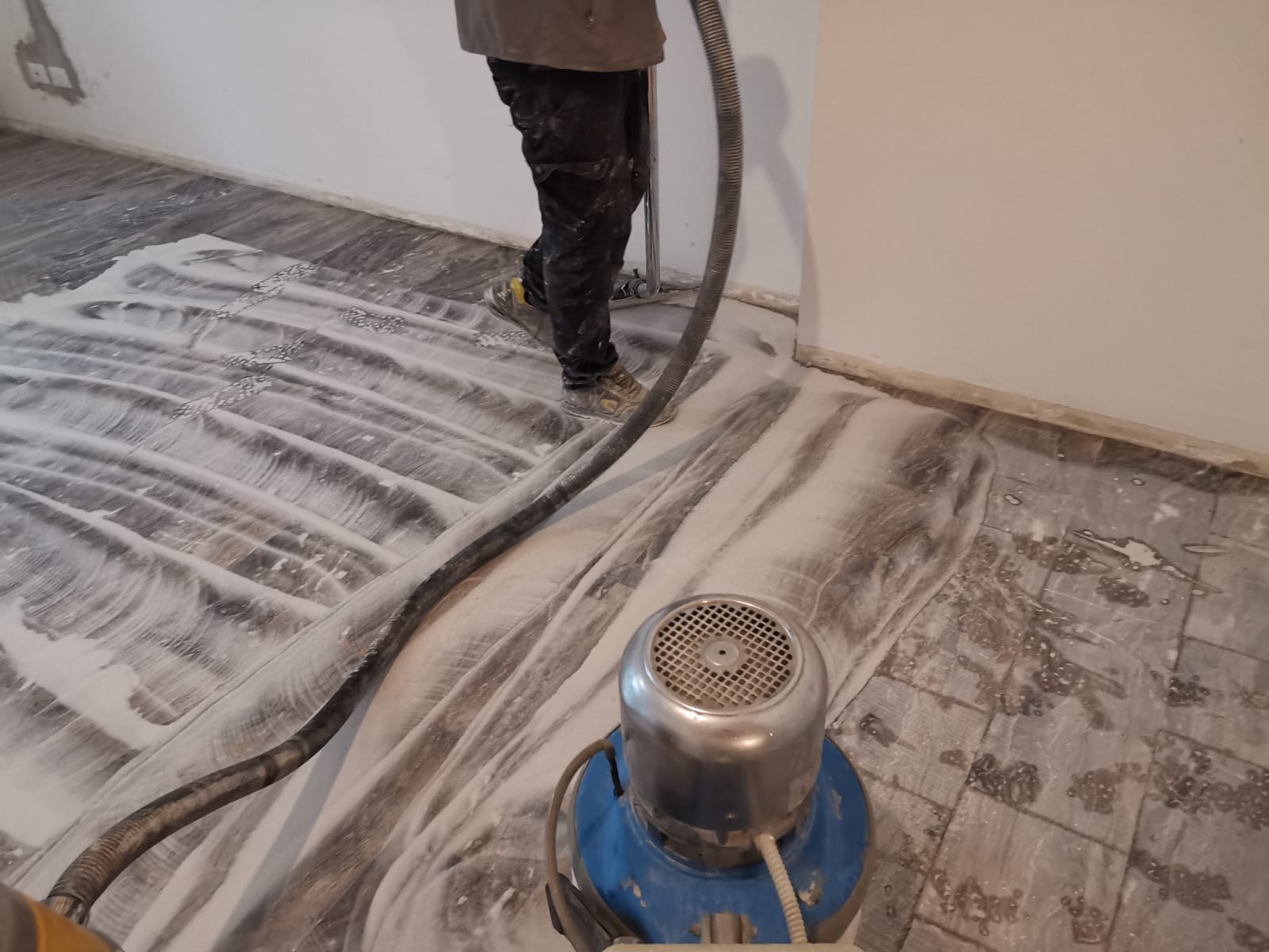 Person sanding a wooden floor, using a floor buffer, with a white dusty residue.