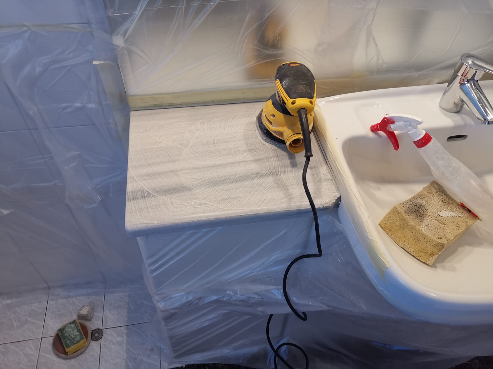 A yellow sander on a countertop near a sink, covered in plastic sheeting.
