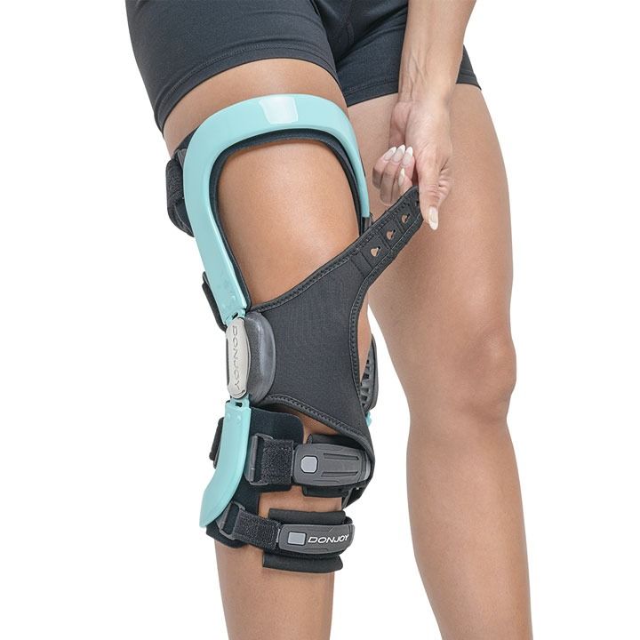 Person wearing a black and teal orthopedic knee brace on a bent leg