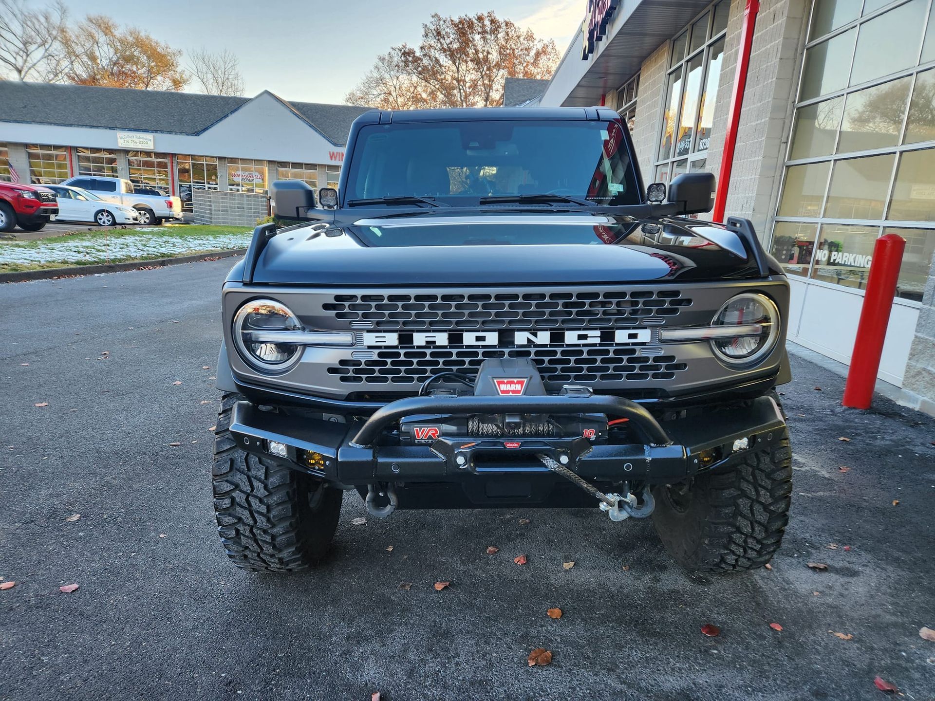 Black Ford Bronco parked outside a building, front view with off-road tires and red posts nearby