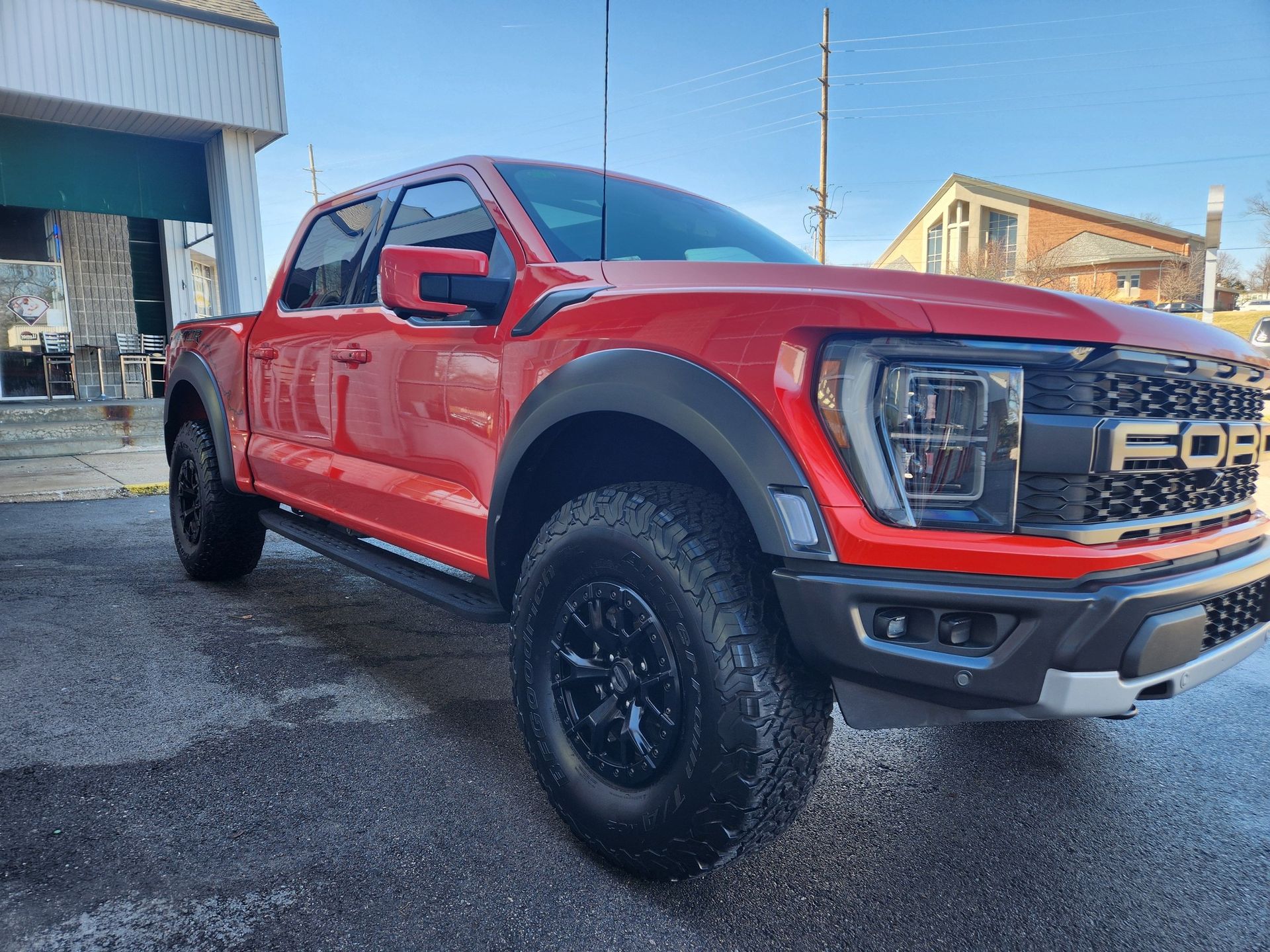 Red Ford pickup truck parked outdoors on a wet lot, side view with black wheels.