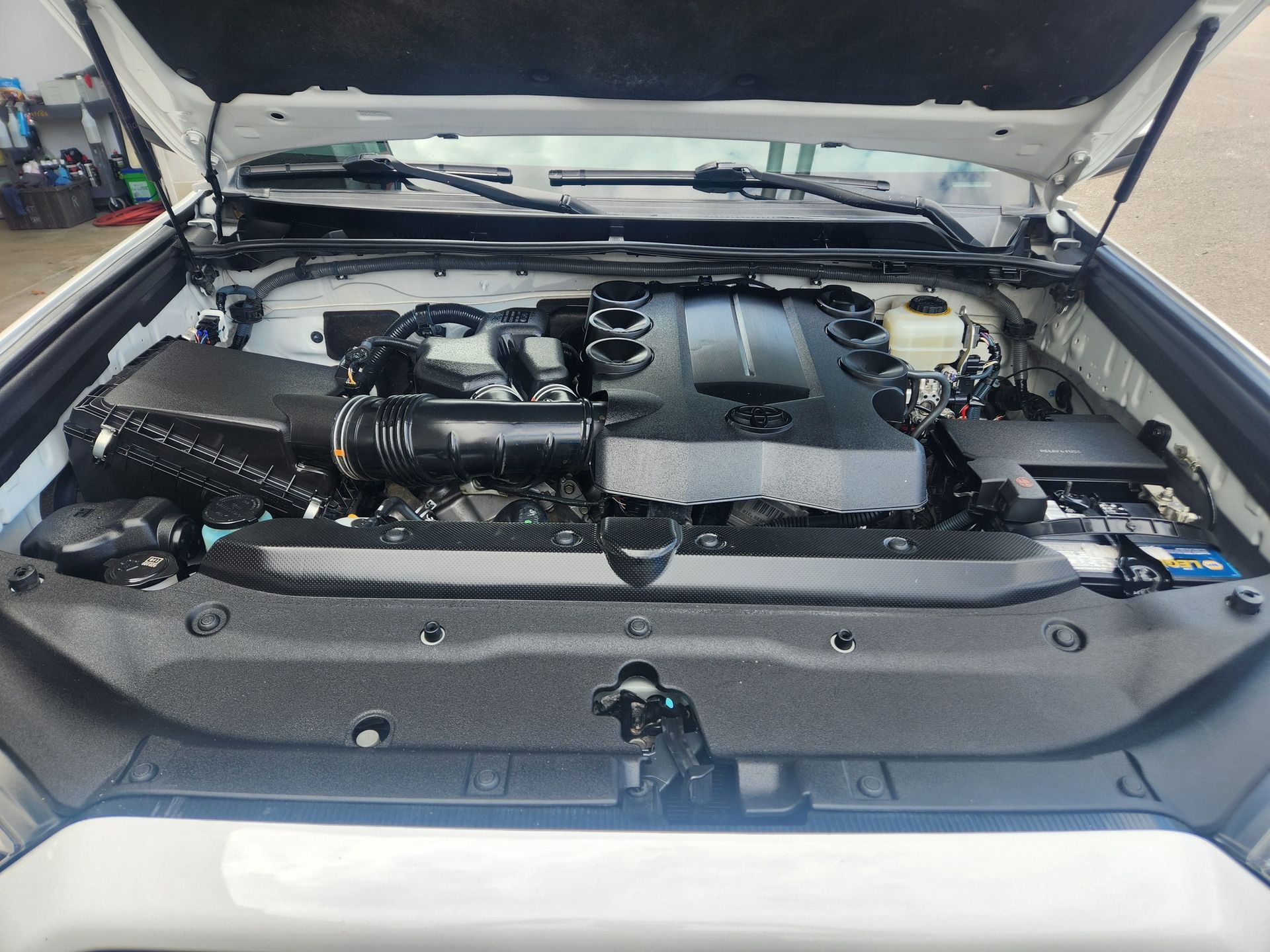 Open car hood showing engine bay with black components and silver trim.