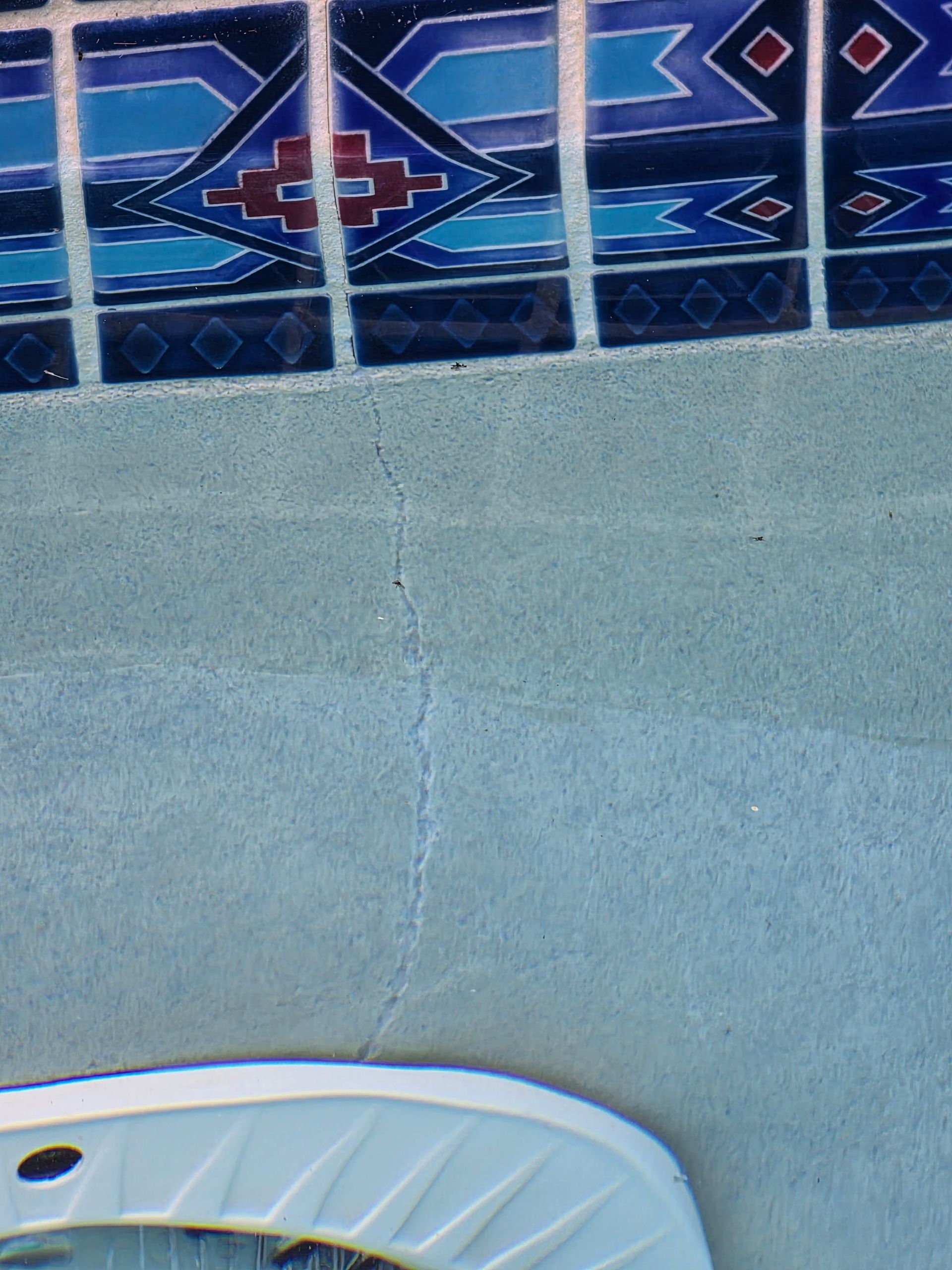 Close-up of leaking pool crack coming up from the pool light into the tile line