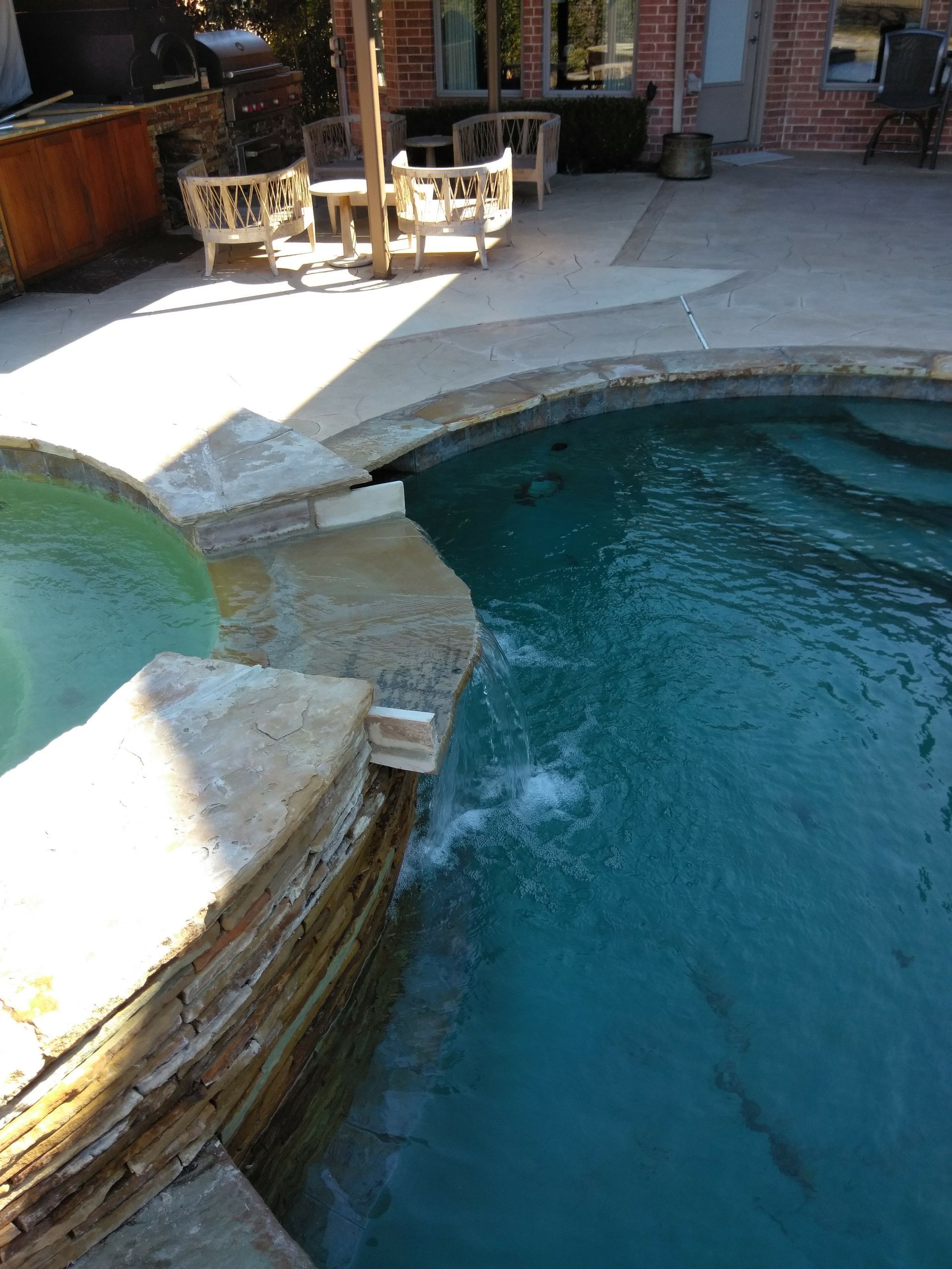 Poolside patio with curved blue swimming pool and lounge chairs in the shade