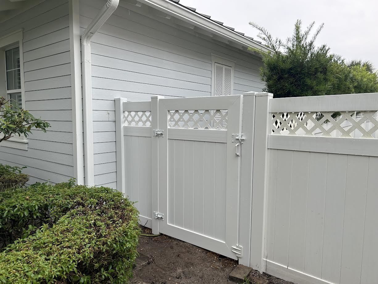 A white vinyl gate with lattice detail on the top, installed between a white-sided house and a matching privacy fence.
