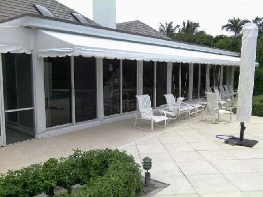 A patio featuring white outdoor chairs under a large, extended white retractable awning attached to a house.