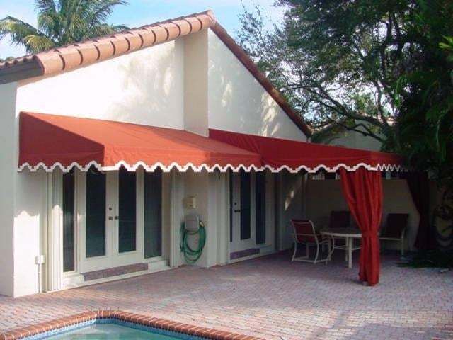 Red fabric awning with a scalloped white edge over a patio next to a swimming pool.