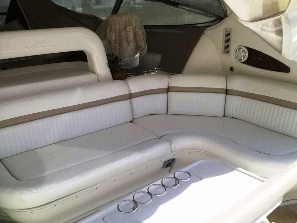 U-shaped white boat seating with beige trim around a central table with drink holders, set inside a boat cockpit.