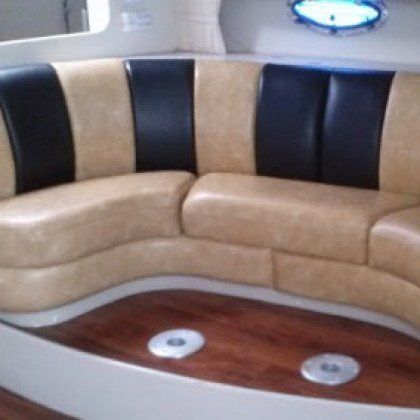 A curved, two-tone tan and black leather boat sofa set against a dark wood floor with two circular base mounts.