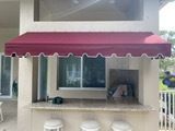 A deep red fabric awning with a scalloped white trim over an outdoor patio bar area with three white stools.