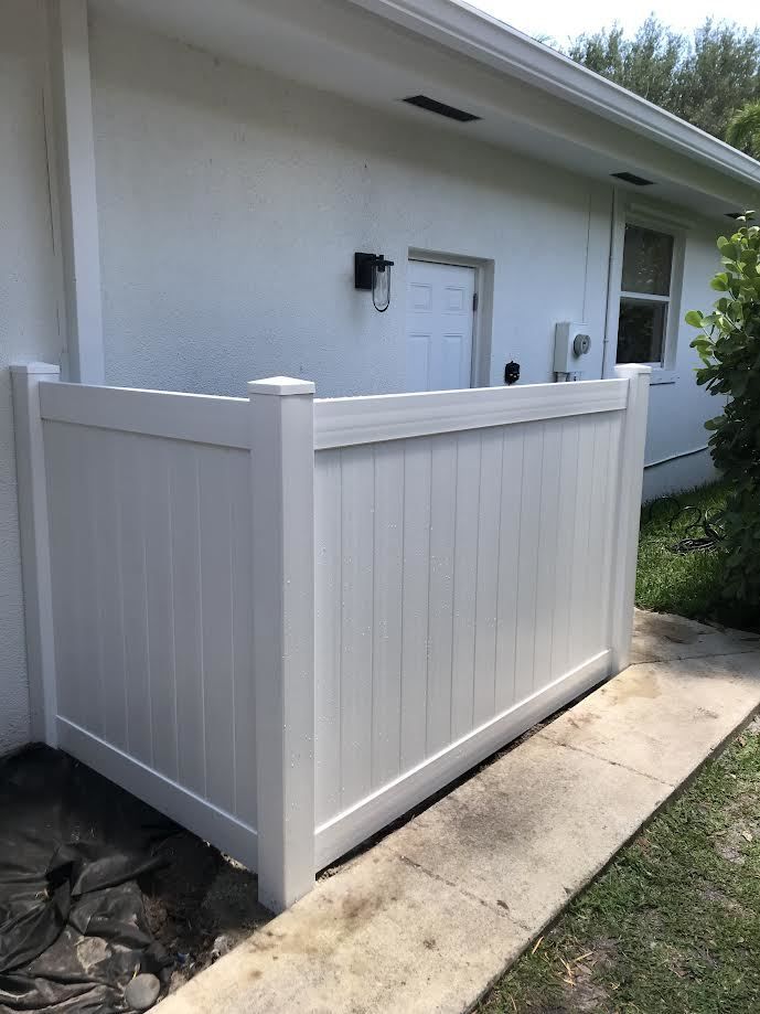 A white vinyl privacy fence screen installed in front of a white building exterior on a paved walkway.